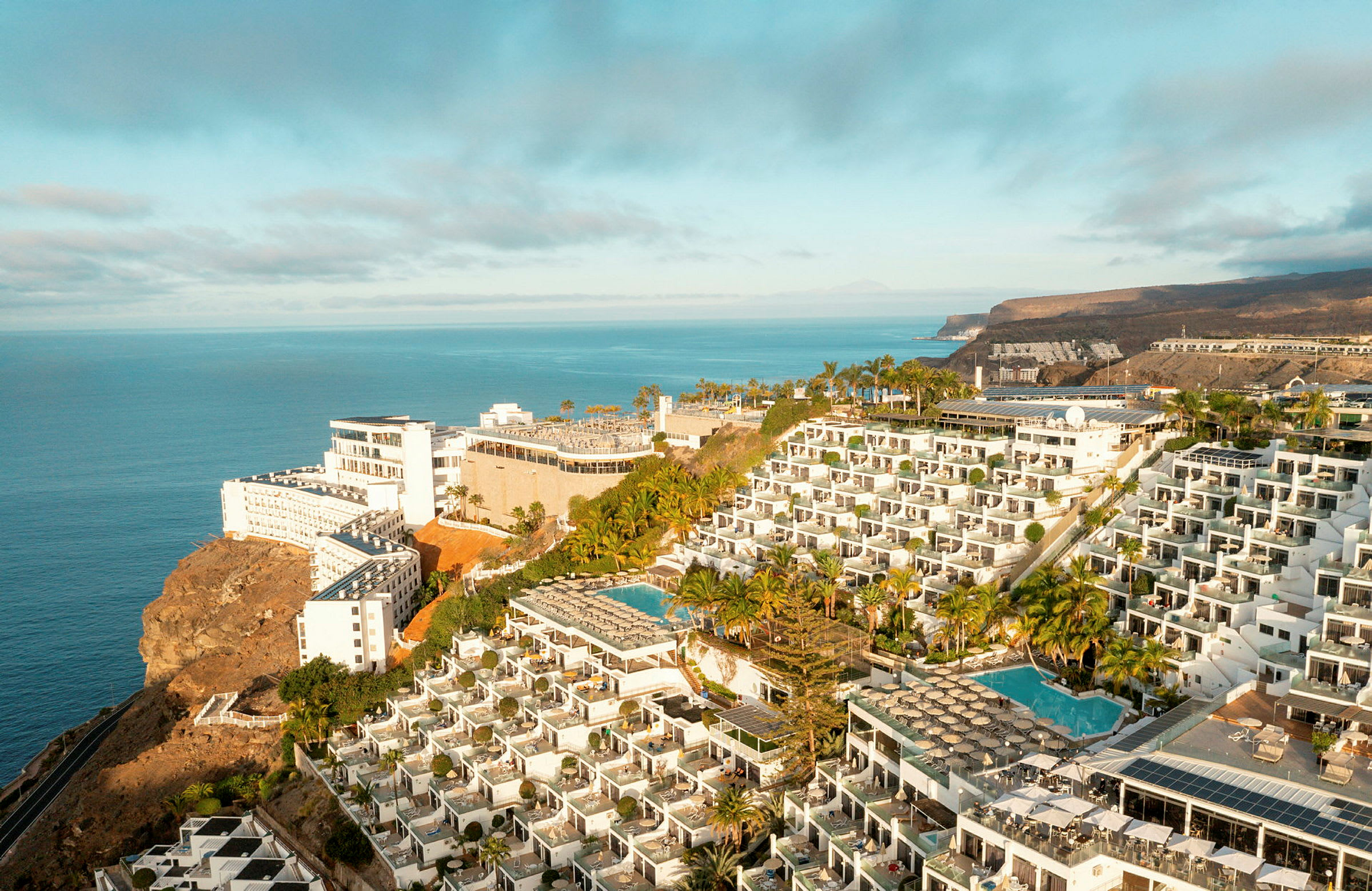 Hotellkompleks på en klippe med bassenger og havutsikt. (AI-generert tekst)