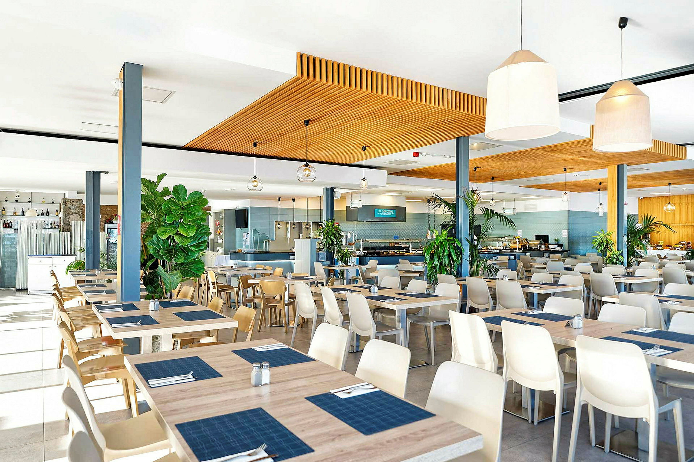 En restaurant med moderne møbler samt bord og stoler. Dekorasjoner inkluderer store potteplanter. (AI-generert tekst)
