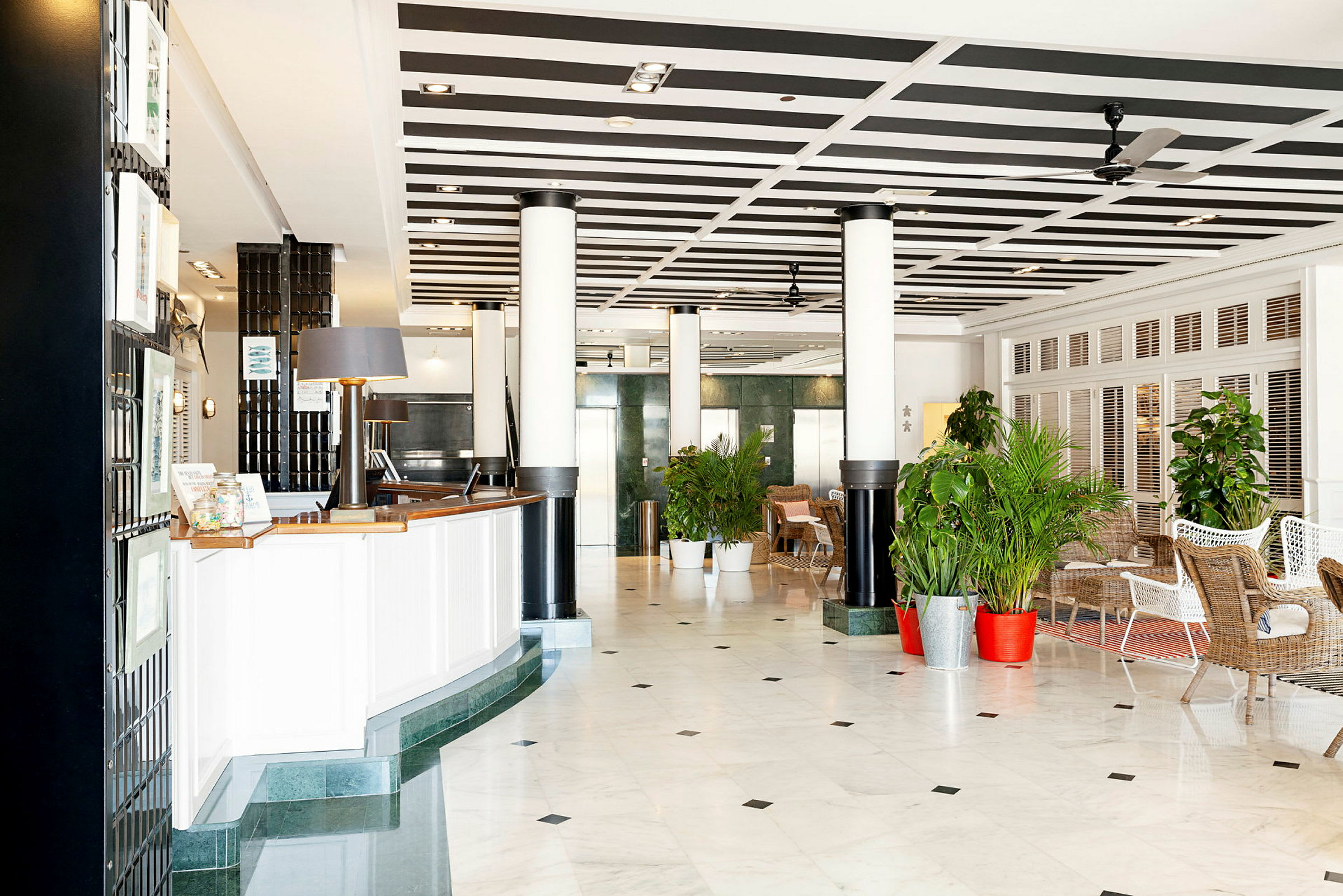Hotellobby med resepsjon og sittegrupper, omgitt av planter. (AI-generert tekst)