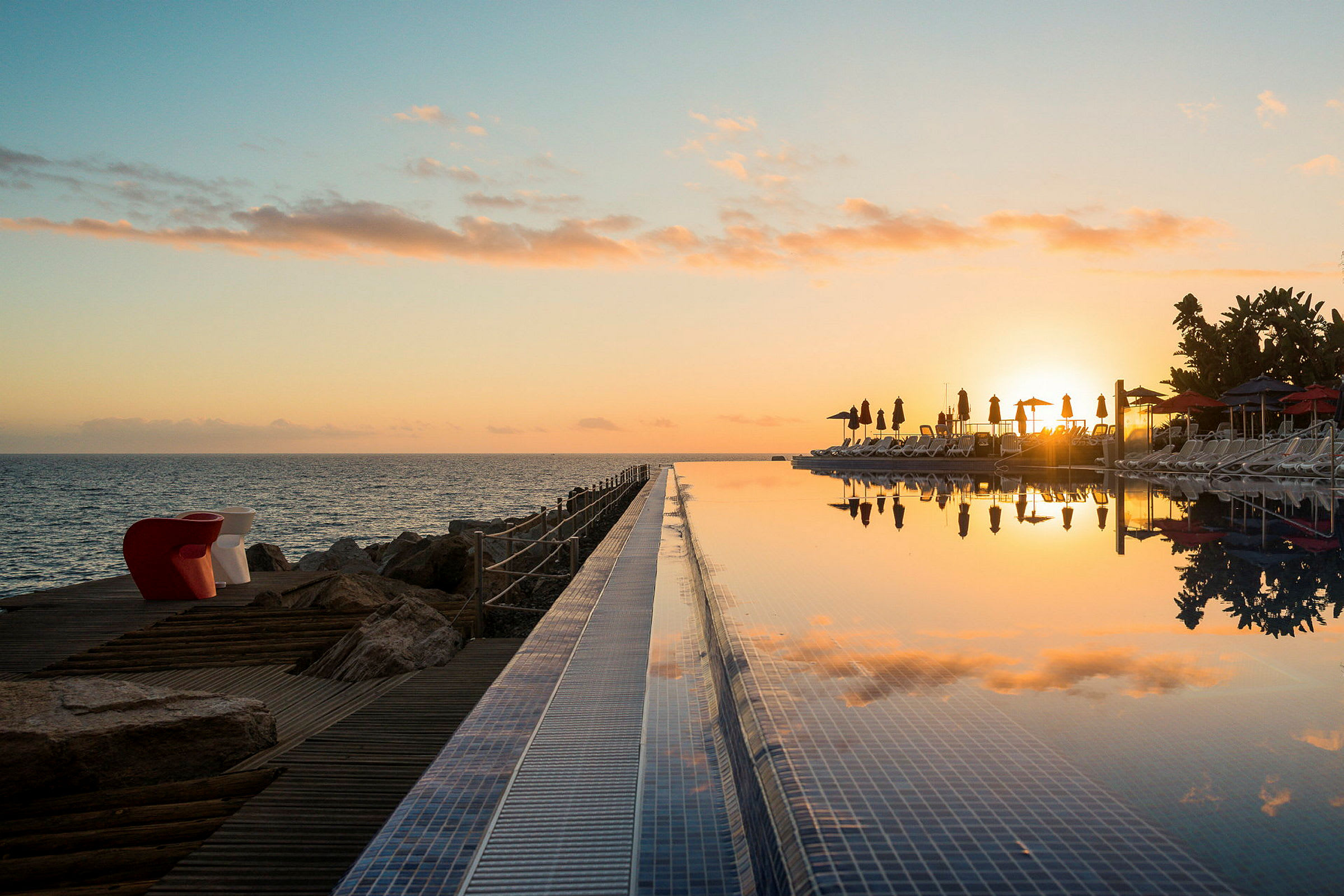 Solnedgang over havet og et infinitybasseng med solsenger. (AI-generert tekst)