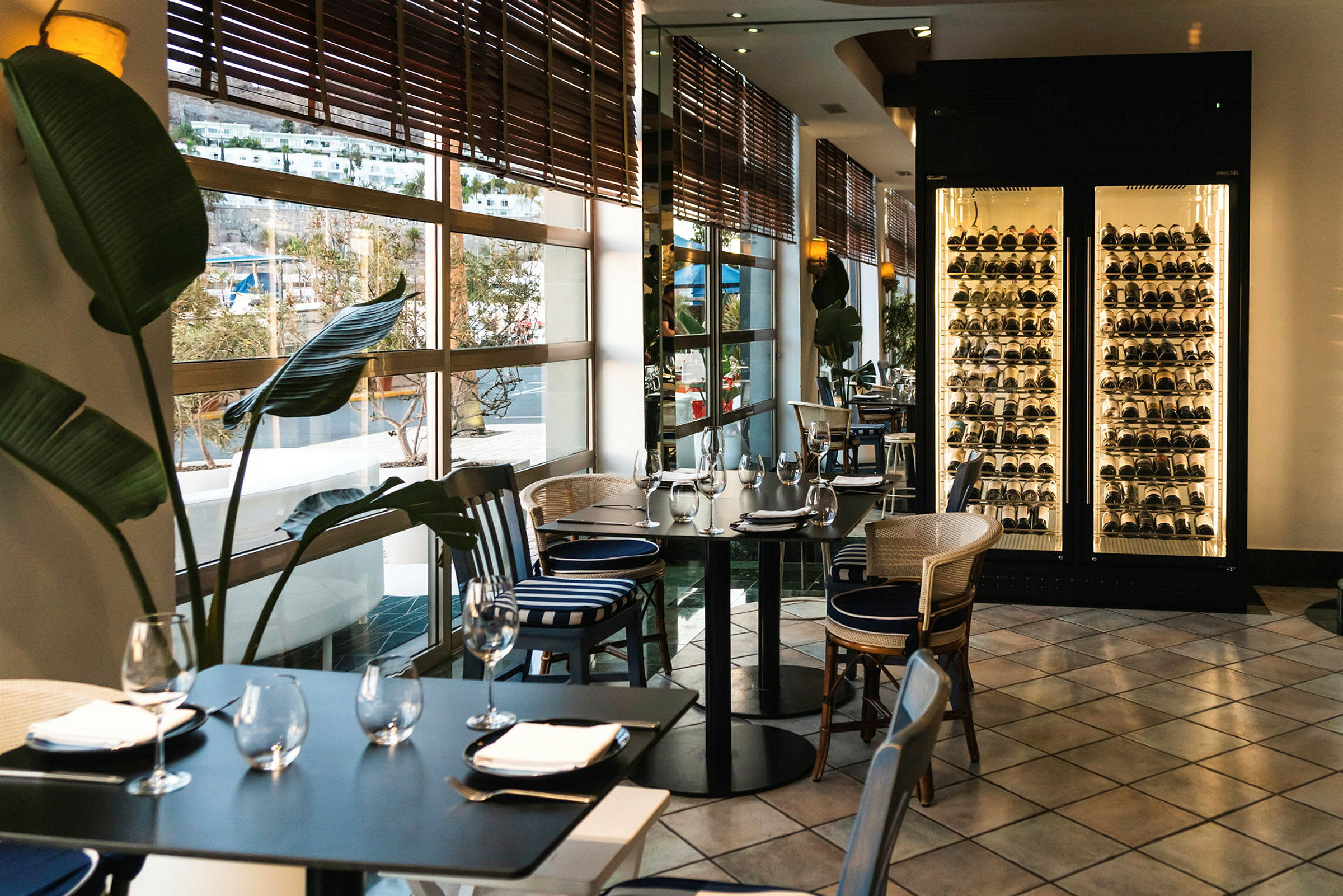 Interiør av en restaurant med dekkede bord, store vinduer med utsikt og opplyst vinlagring. (AI-generert tekst)