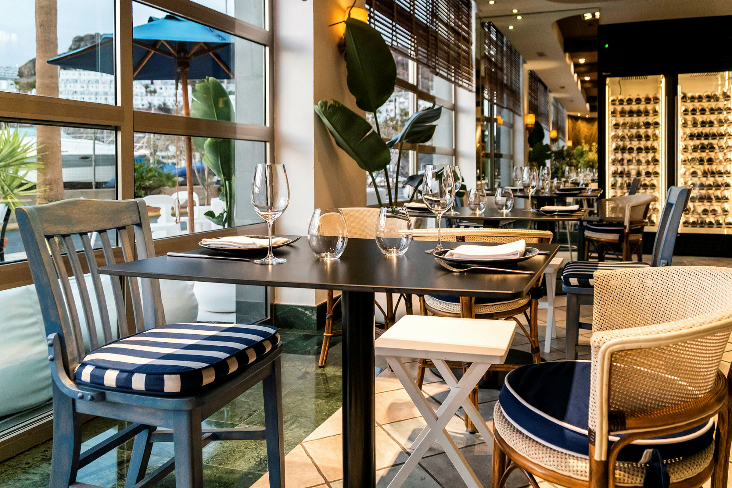 Elegant restaurant med dekkede bord og stoler nær store vinduer. (AI-generert tekst)