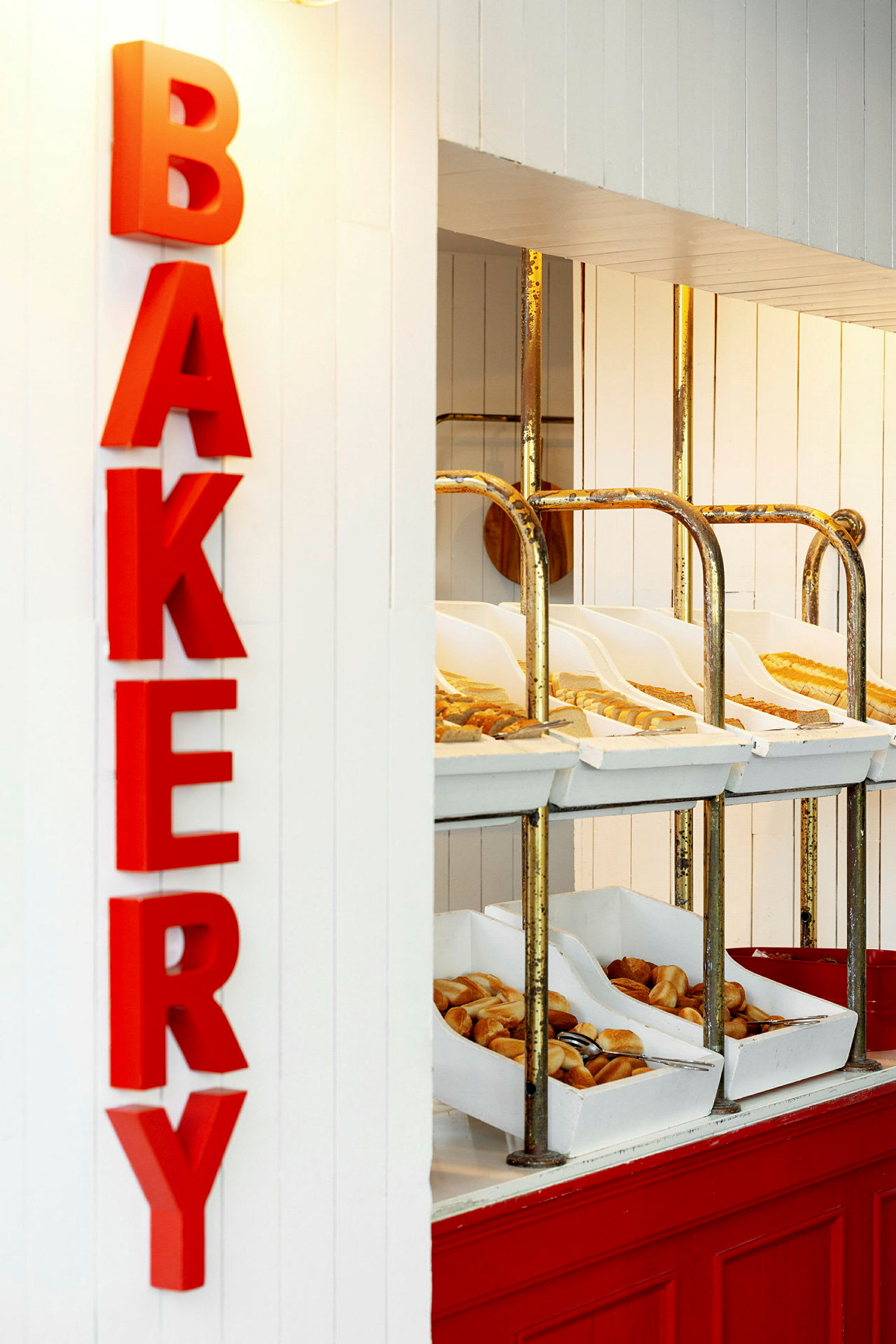 Et bakeriområde med røde bokstaver som staver ordet 'BAKERY'. Hyller inneholder ulike typer brød og bakverk i hvite bokser. (AI-generert tekst)
