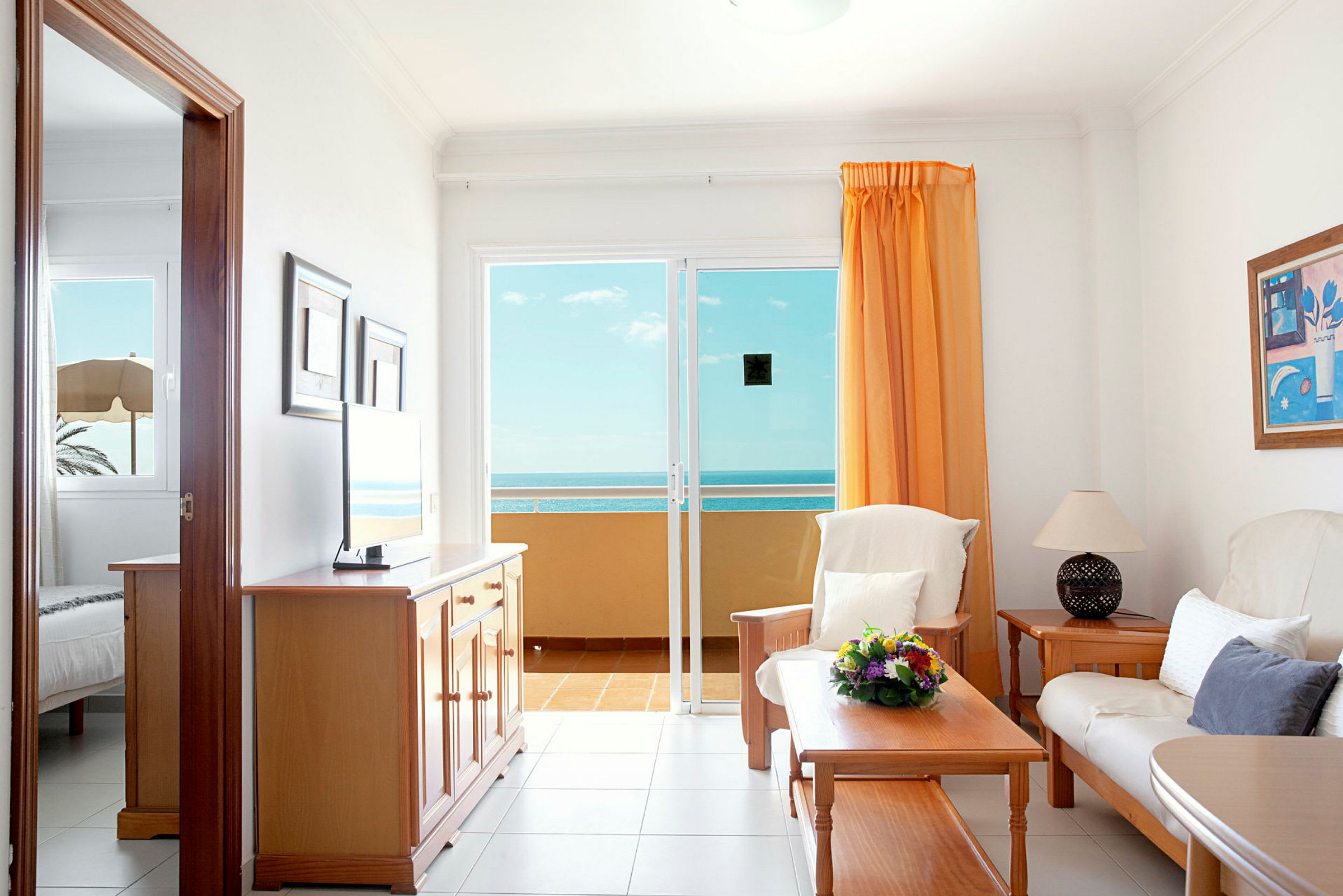 En stue med sofa, bord og utsikt over havet fra en glassdør. (AI-generert tekst)
