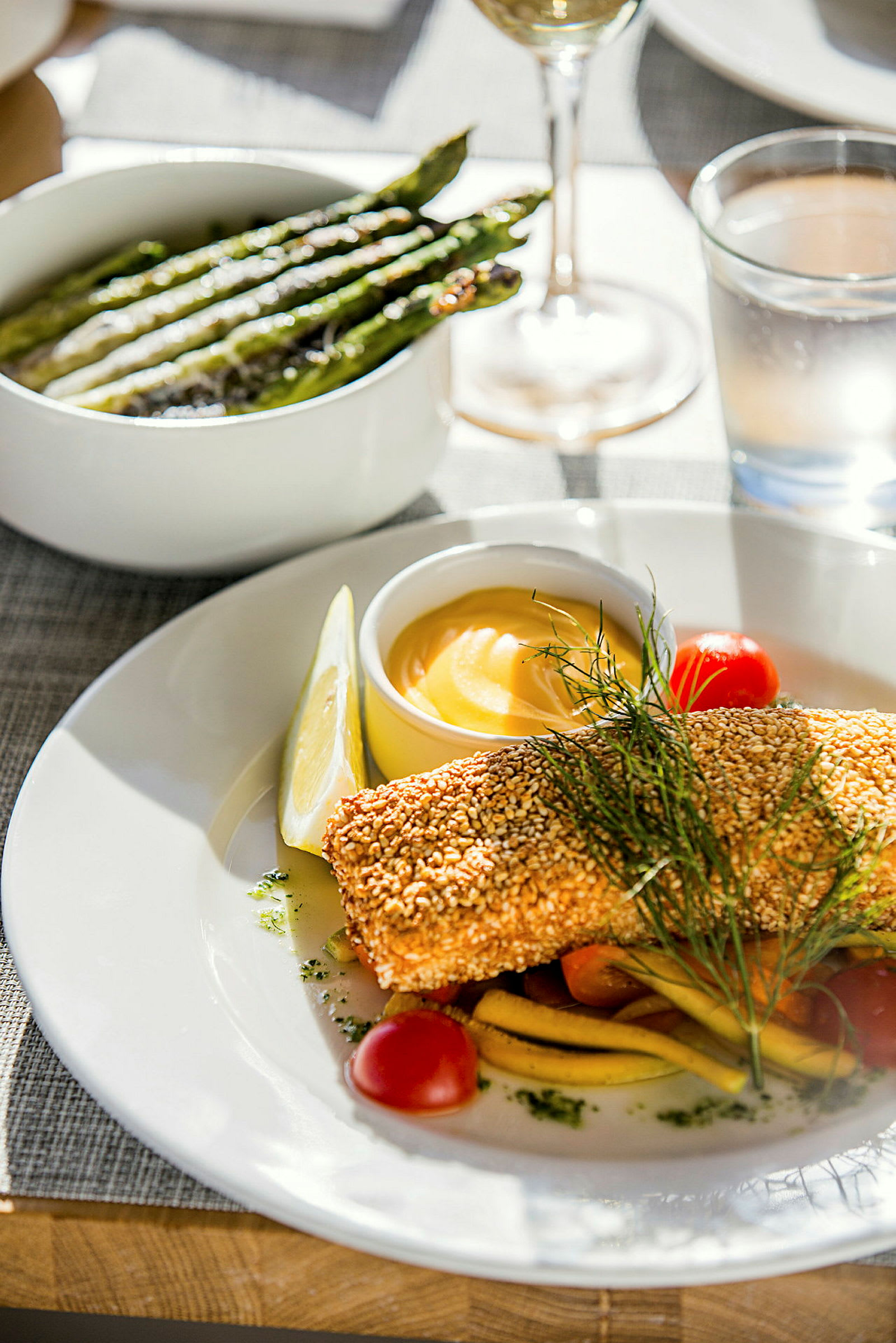 En tallerken med sesamstekt fisk, grønnsaker og en bolle med saus, med en skål med grillet asparges ved siden av. (AI-generert tekst)