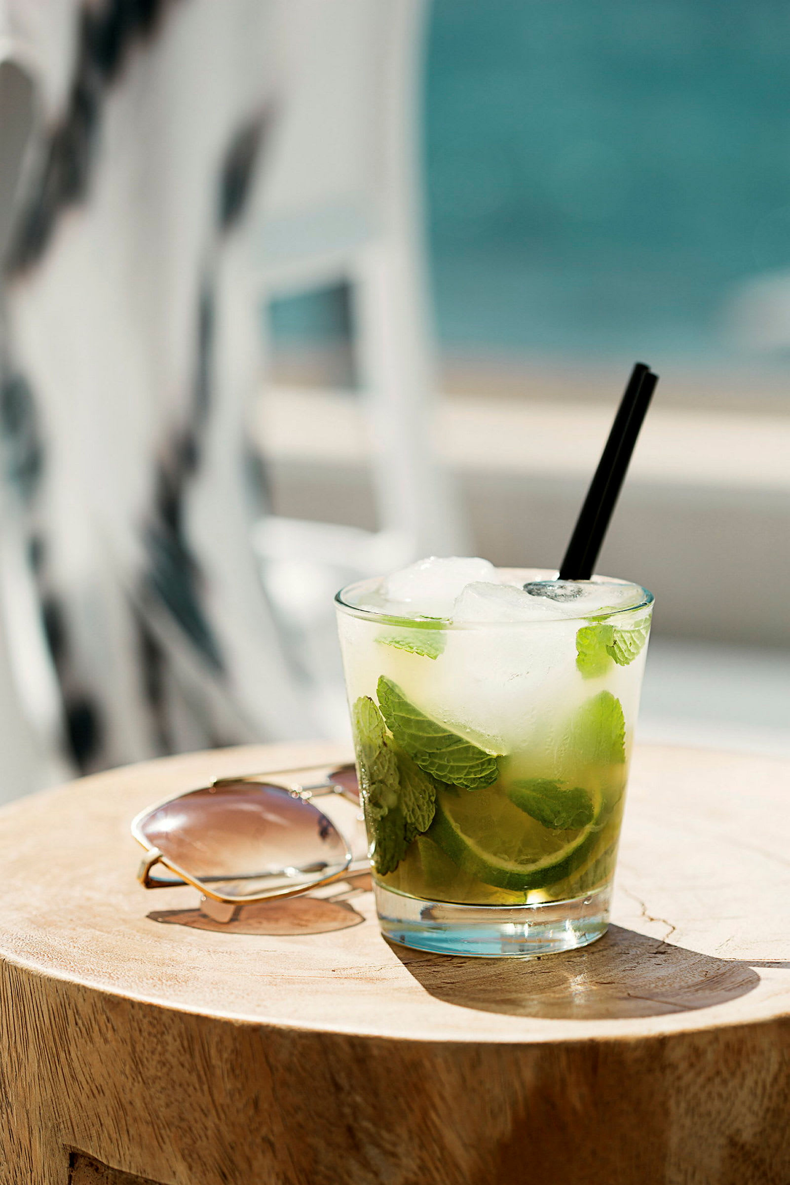 Et glass med lime og mynte ved siden av et par solbriller på et trebord. (AI-generert tekst)