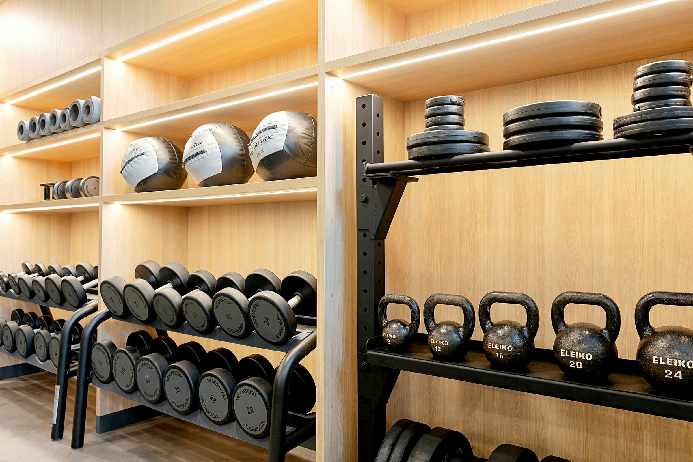 Hylle med ulike treningsutstyr som manualer, kettlebells og vektskiver. (AI-generert tekst)