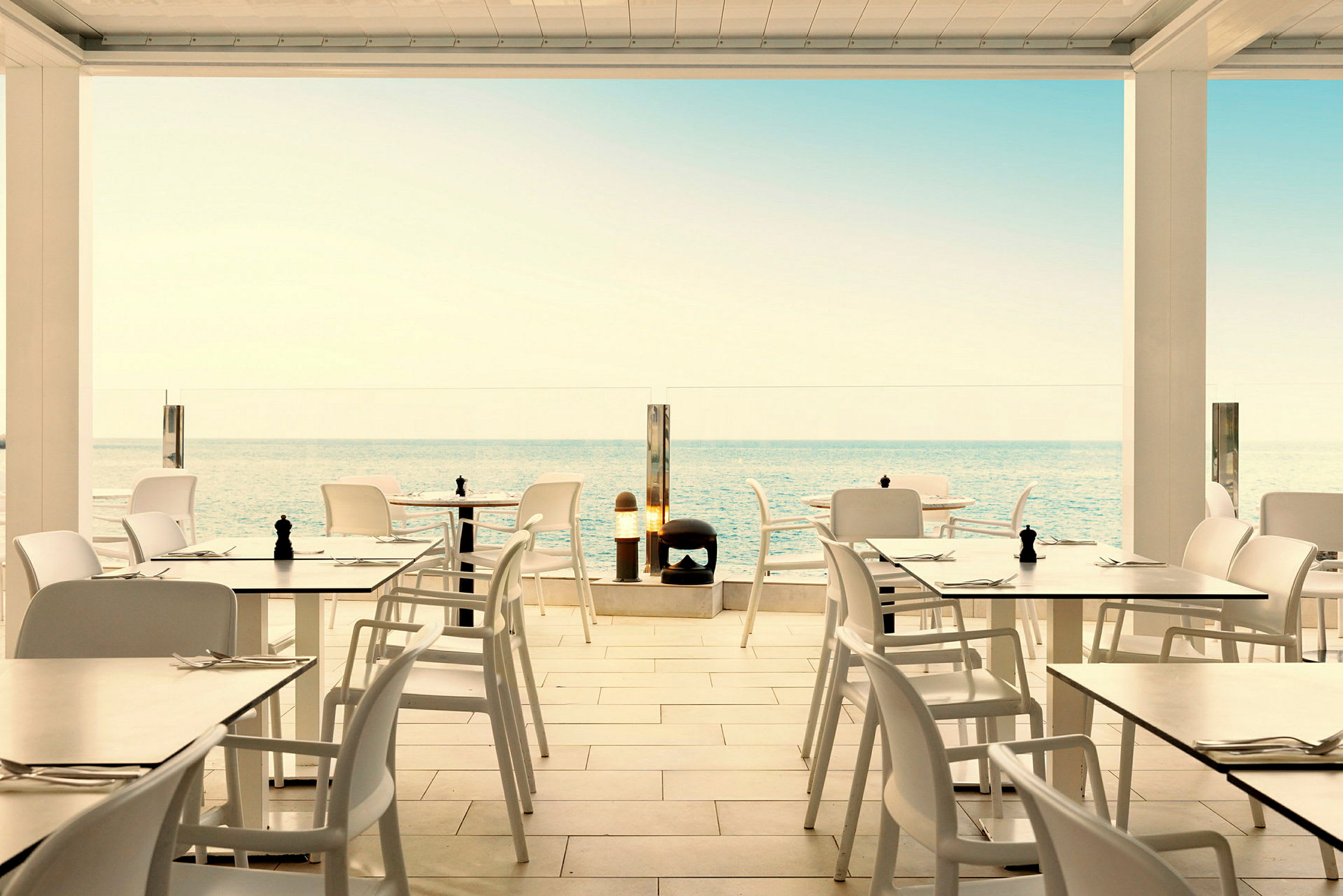 Restaurant med hvite bord og stoler med utsikt over havet. (AI-generert tekst)