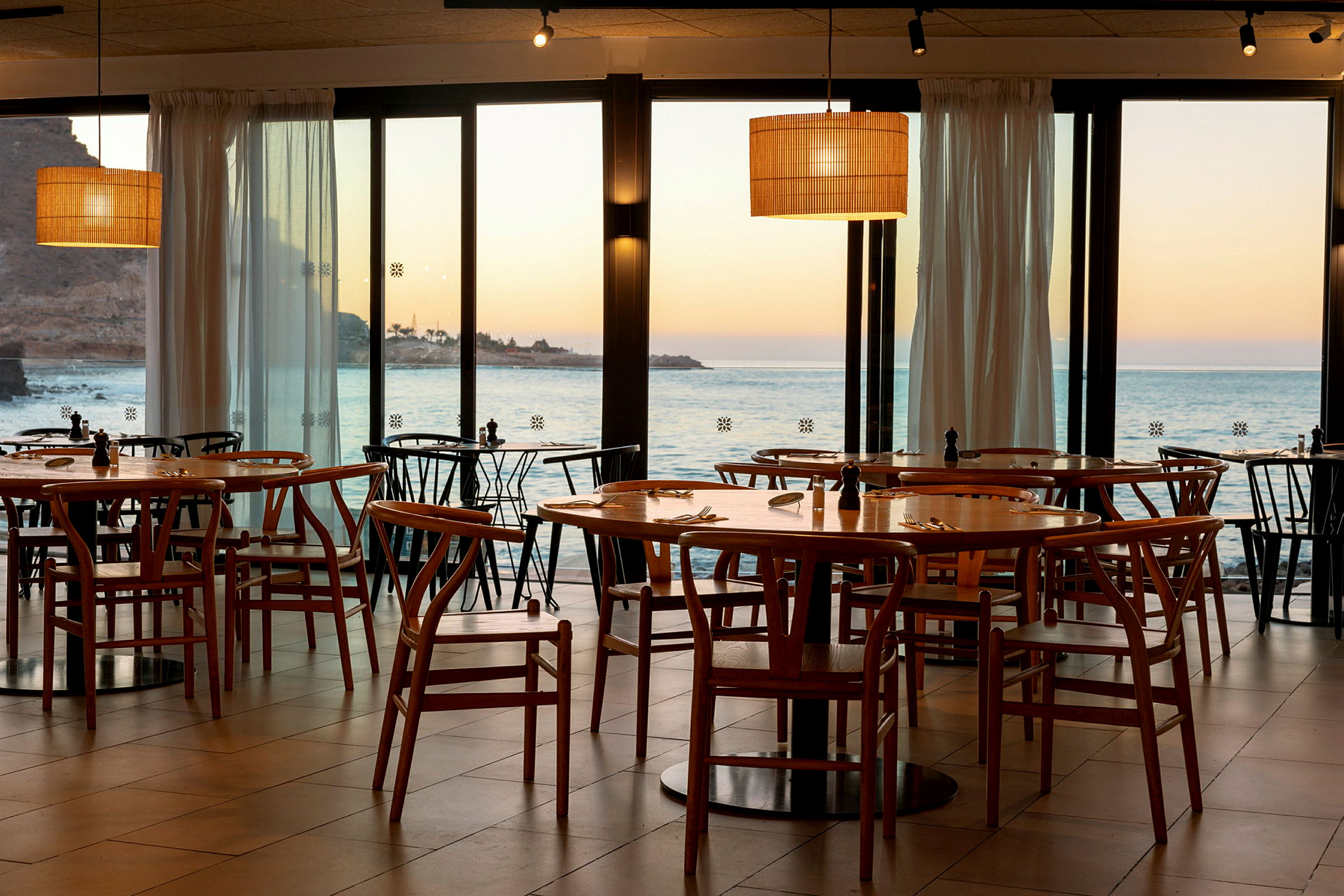 Restaurant med trestoler og bord med utsikt over havet og solnedgang. (AI-generert tekst)