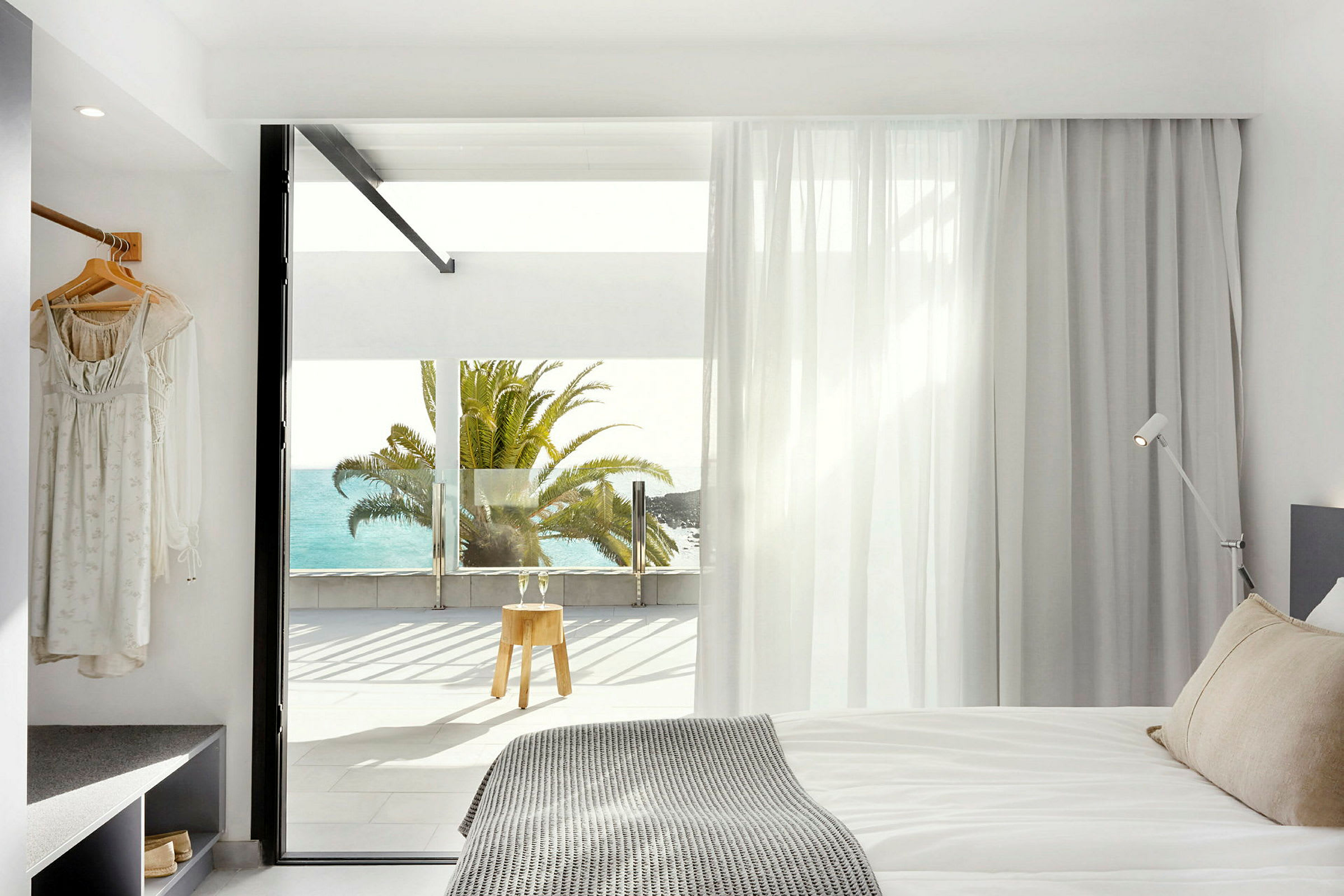 Moderne hotellrom med utsikt mot havet og en palme utenfor vinduet. (AI-generert tekst)