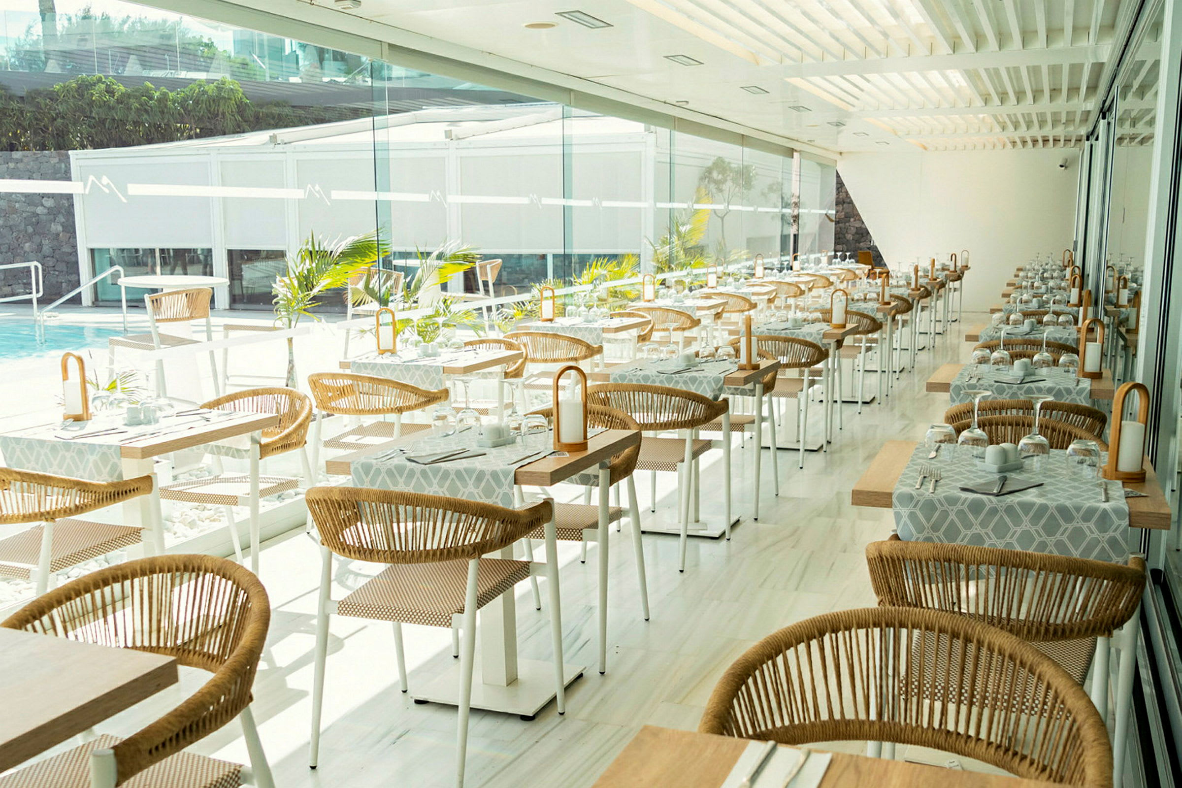 Moderne restaurant med dekkede bord og rottingstoler ved store vinduer. (AI-generert tekst)