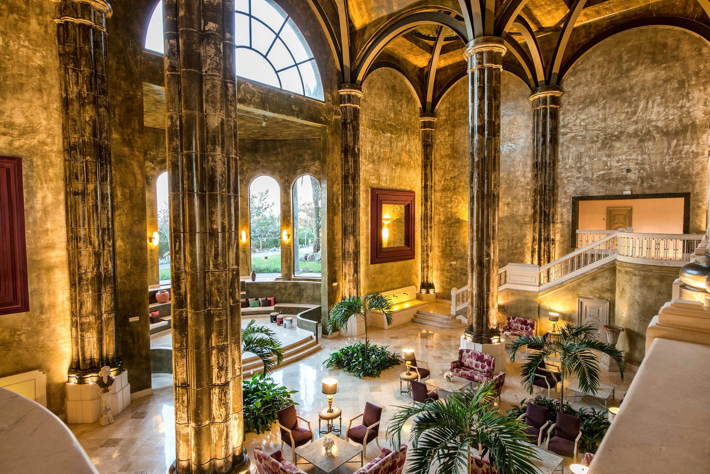 En elegant hotellobby med høye hvelvede tak og store søyler. Vinduer slipper inn naturlig lys. (AI-generert tekst)
