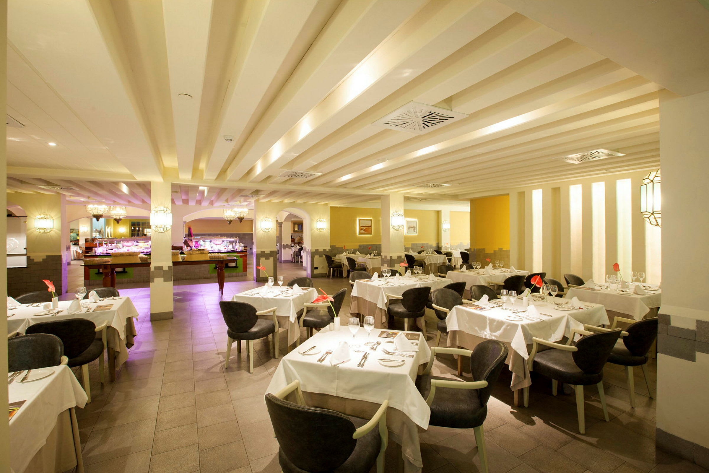 En romslig restaurant med dekkede bord og stoler, opplyst interiør med buffetdisk i bakgrunnen. (AI-generert tekst)