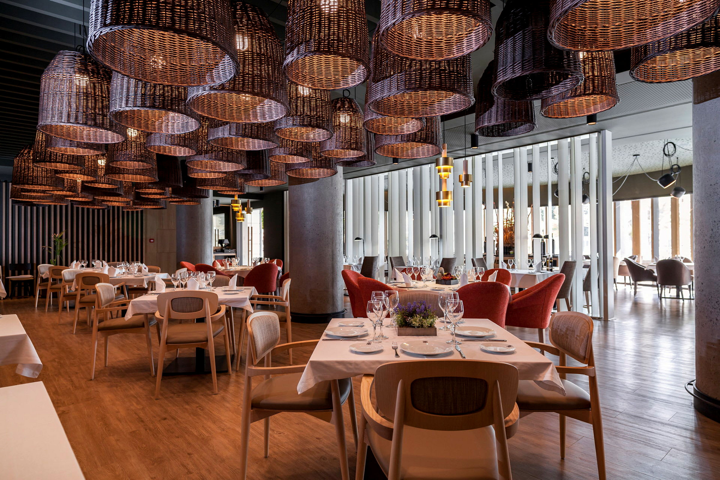 Restaurant med oppdekkede bord, moderne trestoler og store kurvlampeskjermer i taket. (AI-generert tekst)