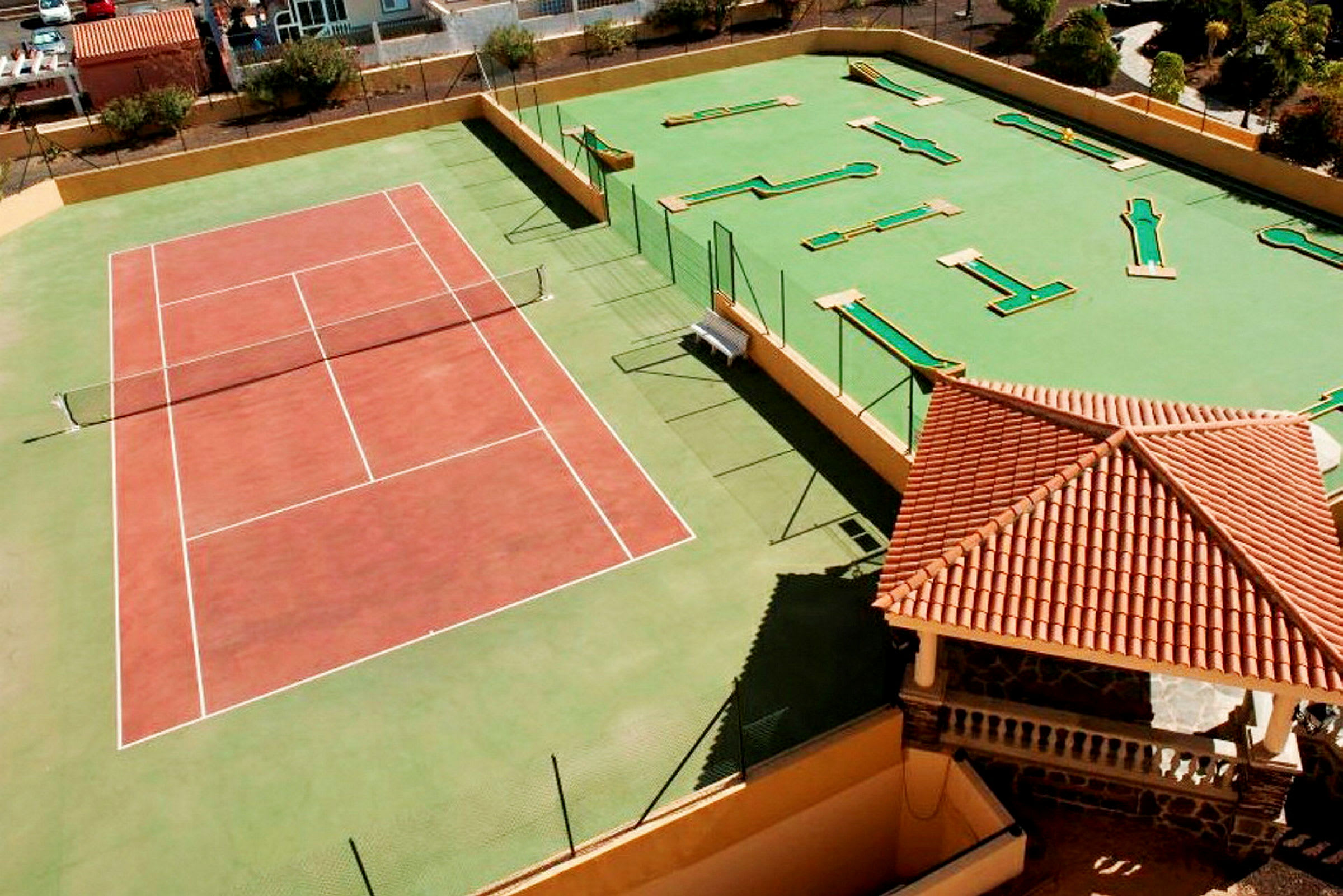 Tennisbane og minigolfområde ved siden av en bygning med rødt tak. (AI-generert tekst)
