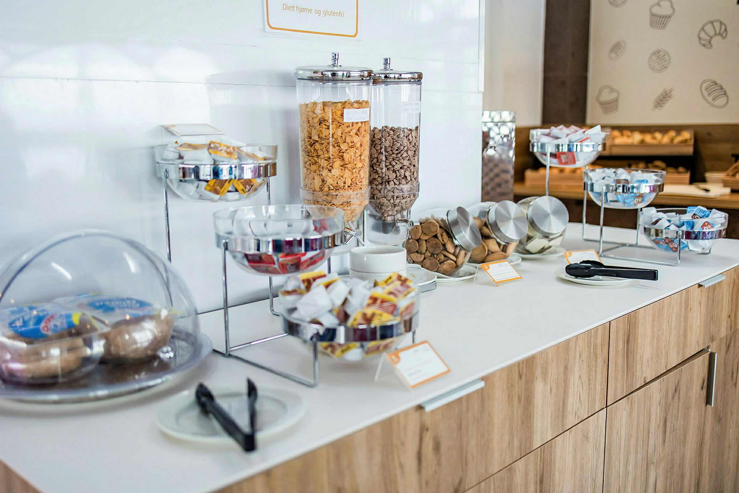 Et matbord med forskjellige frokostalternativer, inkludert frokostblandinger i beholdere og pakket tilbehør. (AI-generert tekst)