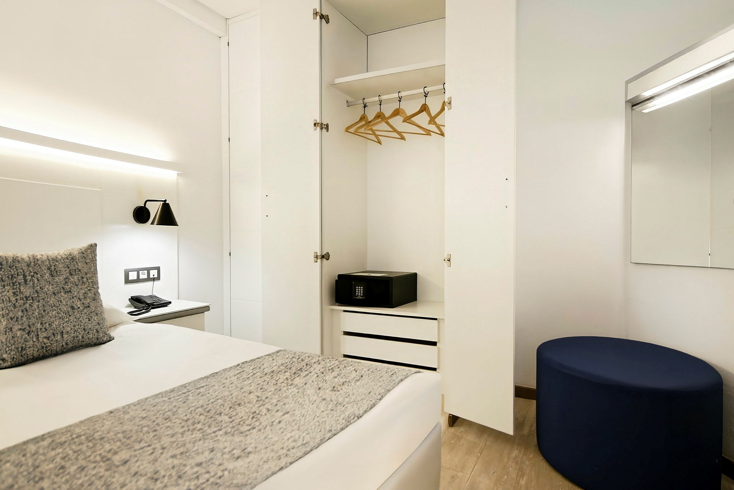 Et hotellrom med åpen garderobe, seng og speil. (AI-generert tekst)