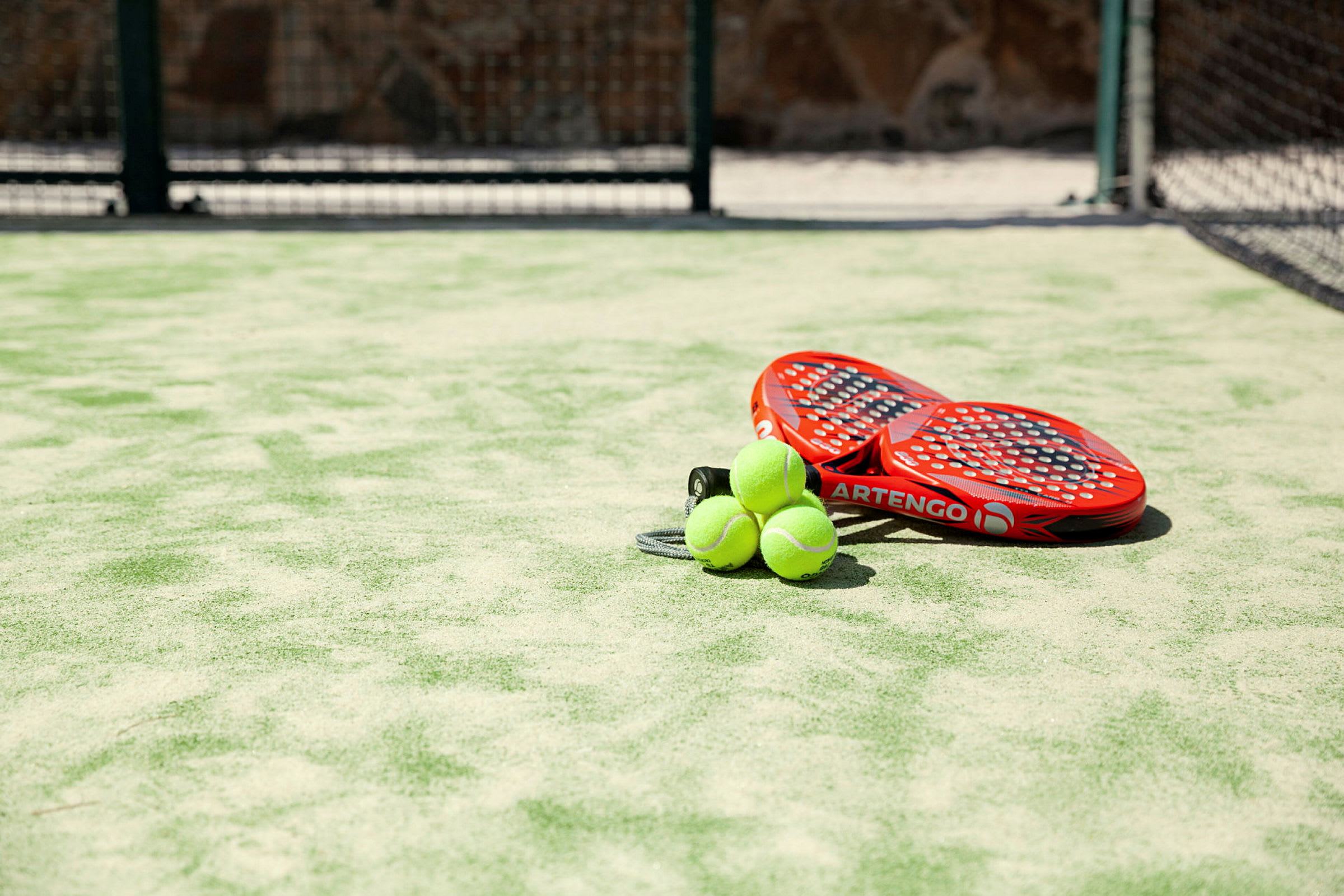 To røde padelracketer og tre grønne baller på en kunstgressbane. (AI-generert tekst)