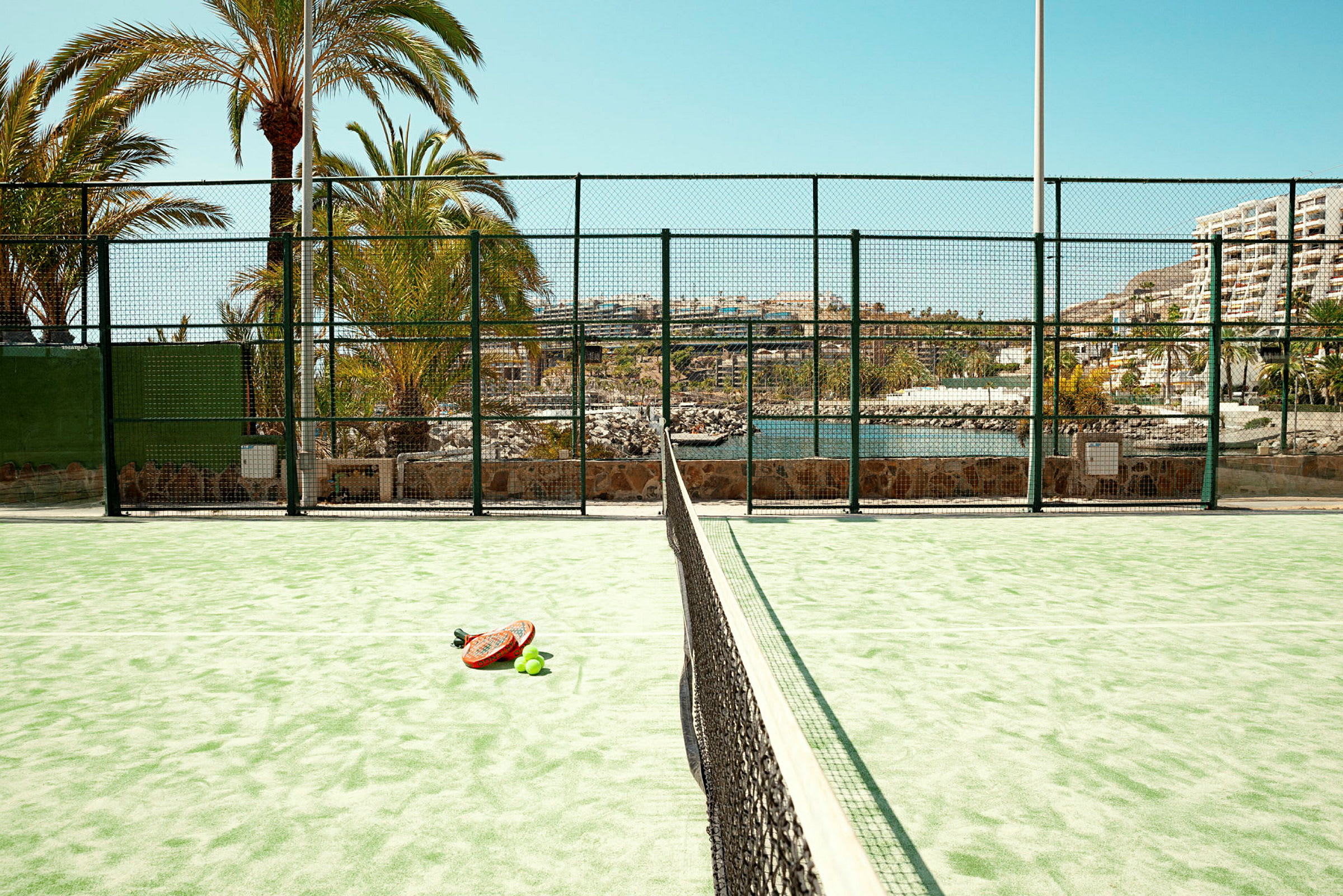 En padelbane med en racket og baller på bakken. (AI-generert tekst)