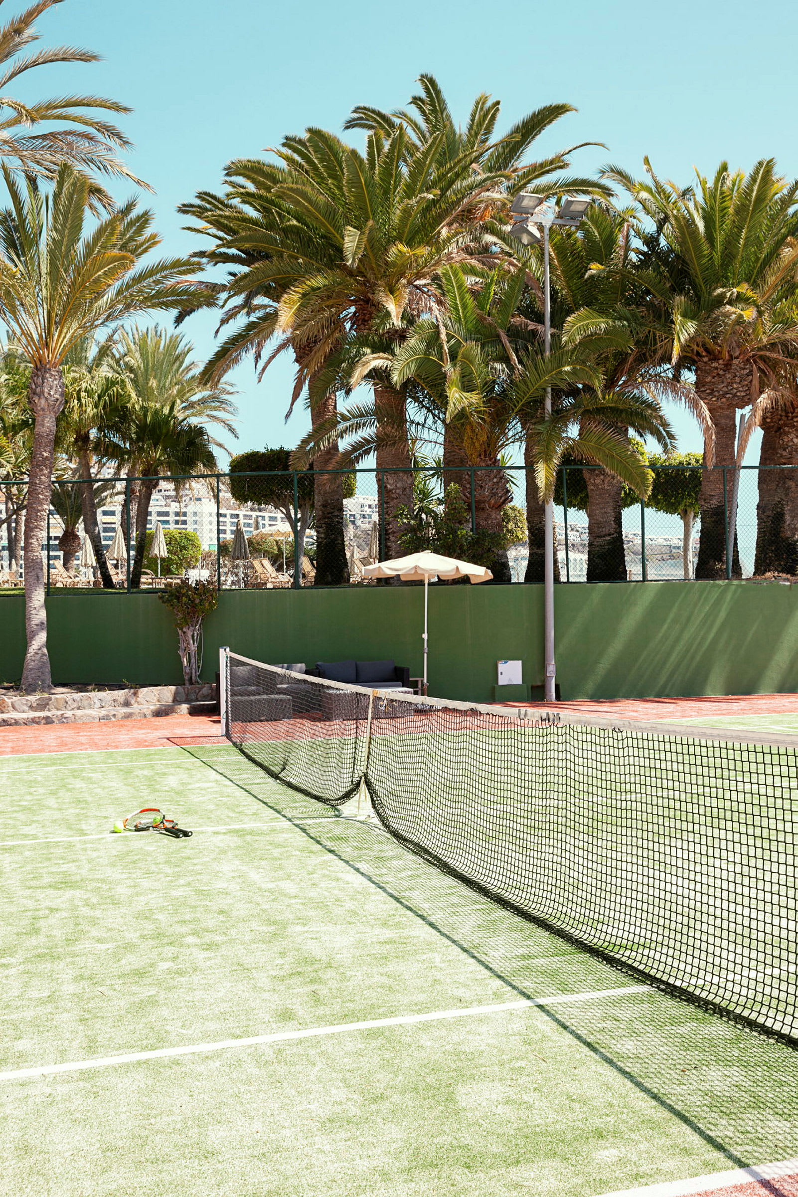 En tennisbane med nett og racketer, omgitt av palmer. (AI-generert tekst)