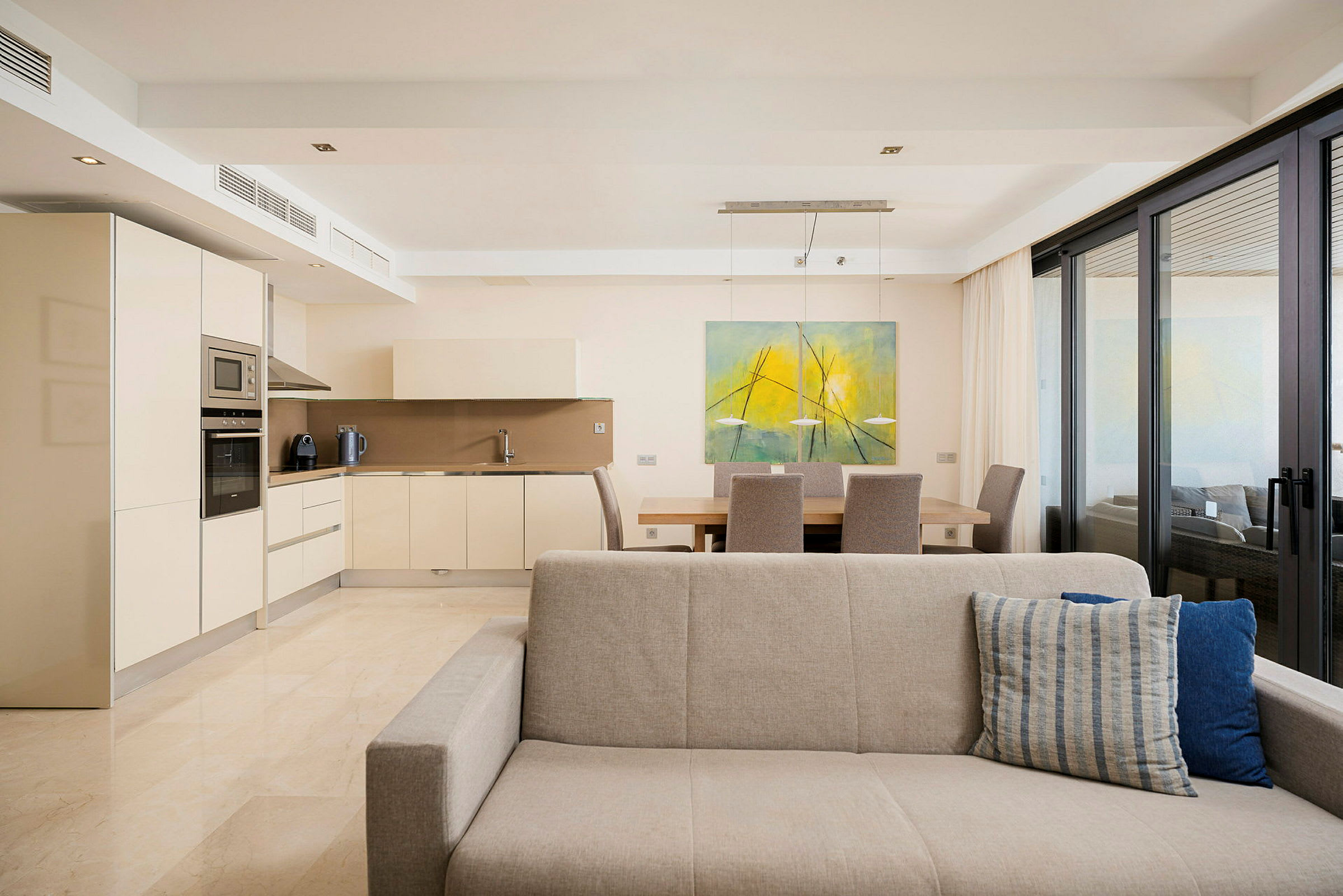Bilde av et moderne kjøkken med beige skap, en spiseplass og en grå sofa i forgrunnen. (AI-generert tekst)
