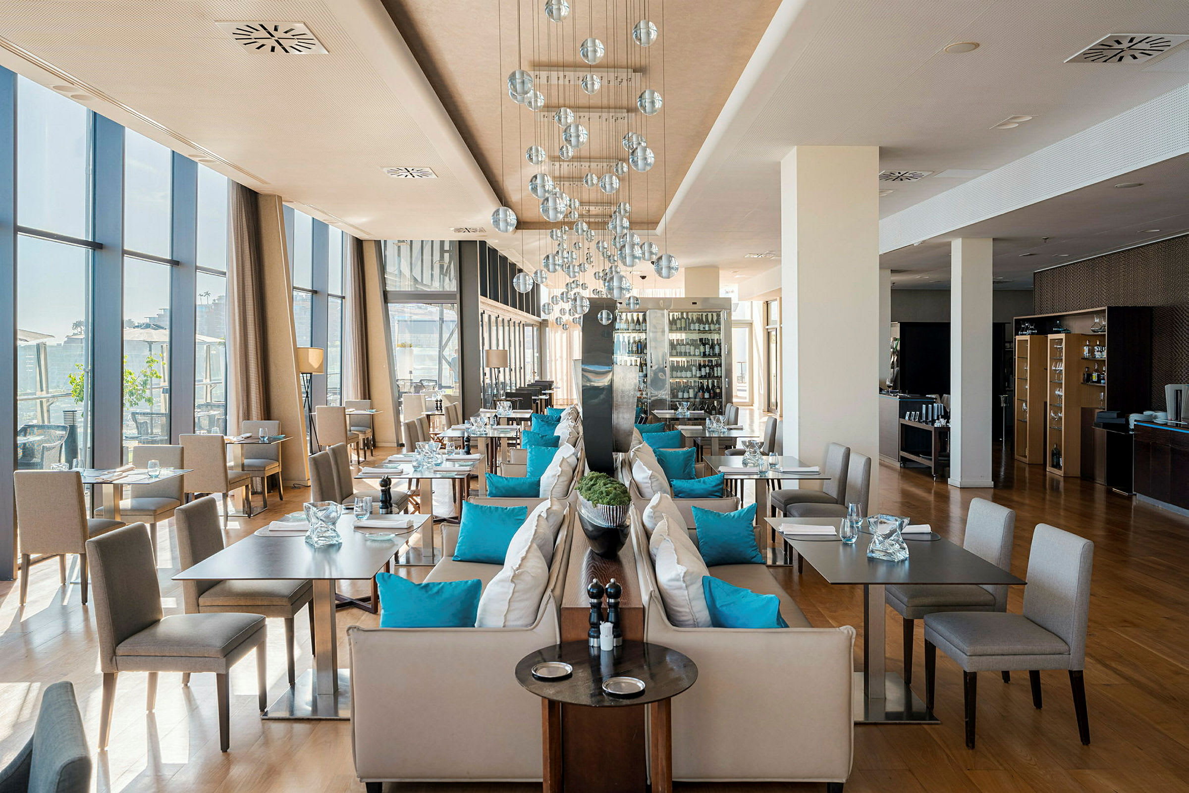 En elegant restaurant med store vinduer, benker dekorert med blå puter og moderne lamper. (AI-generert tekst)