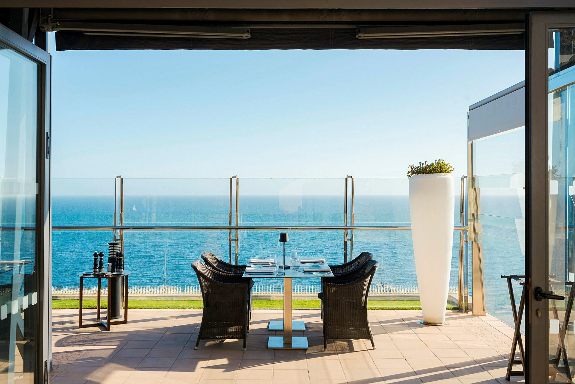 Terrasse med bord, stoler og utsikt over havet. (AI-generert tekst)