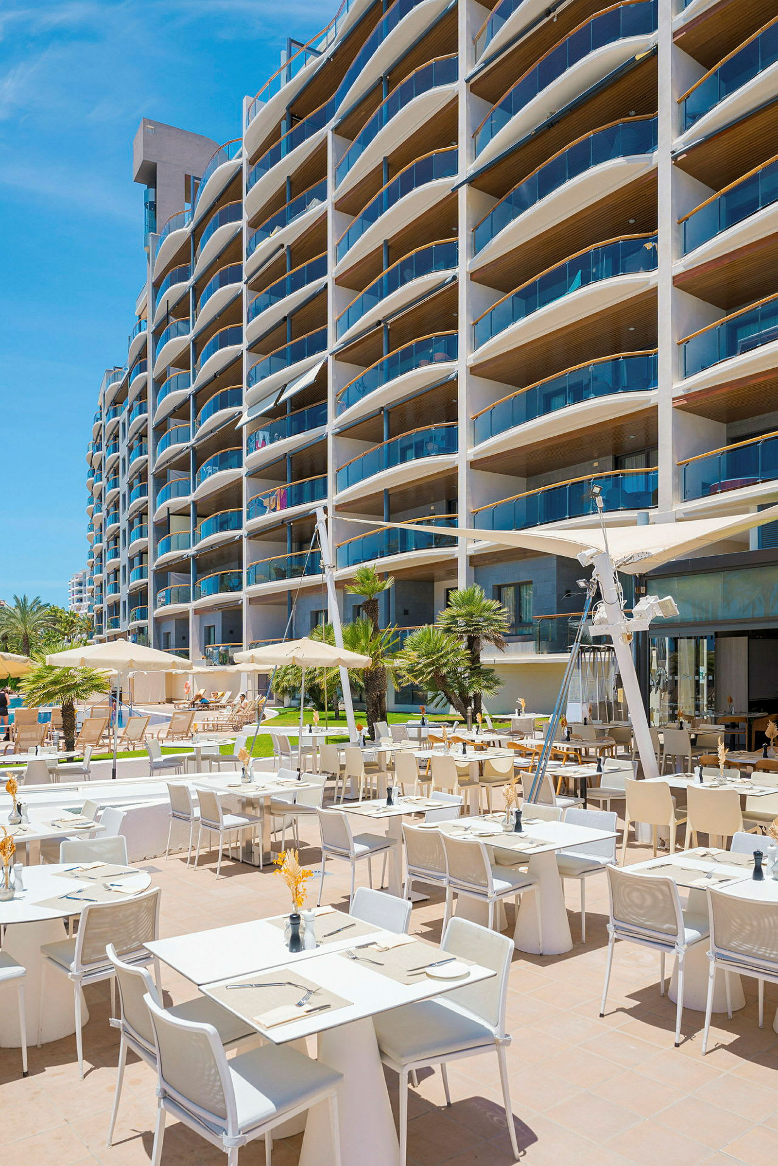 En utendørsrestaurant ved et moderne hotell med mange balkonger. (AI-generert tekst)
