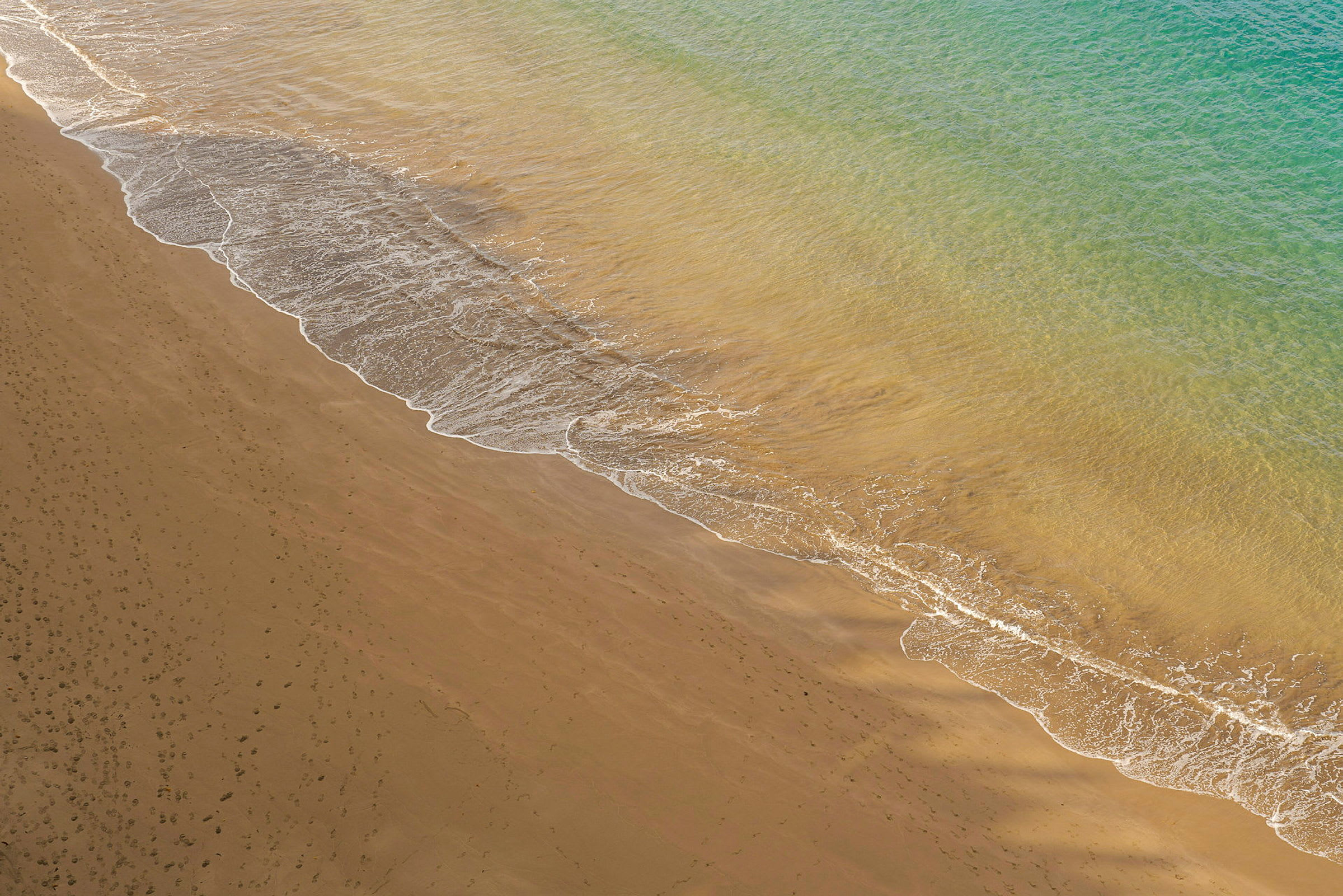 Bildet viser en sandstrand med bølger fra havet som når kanten. (AI-generert tekst)