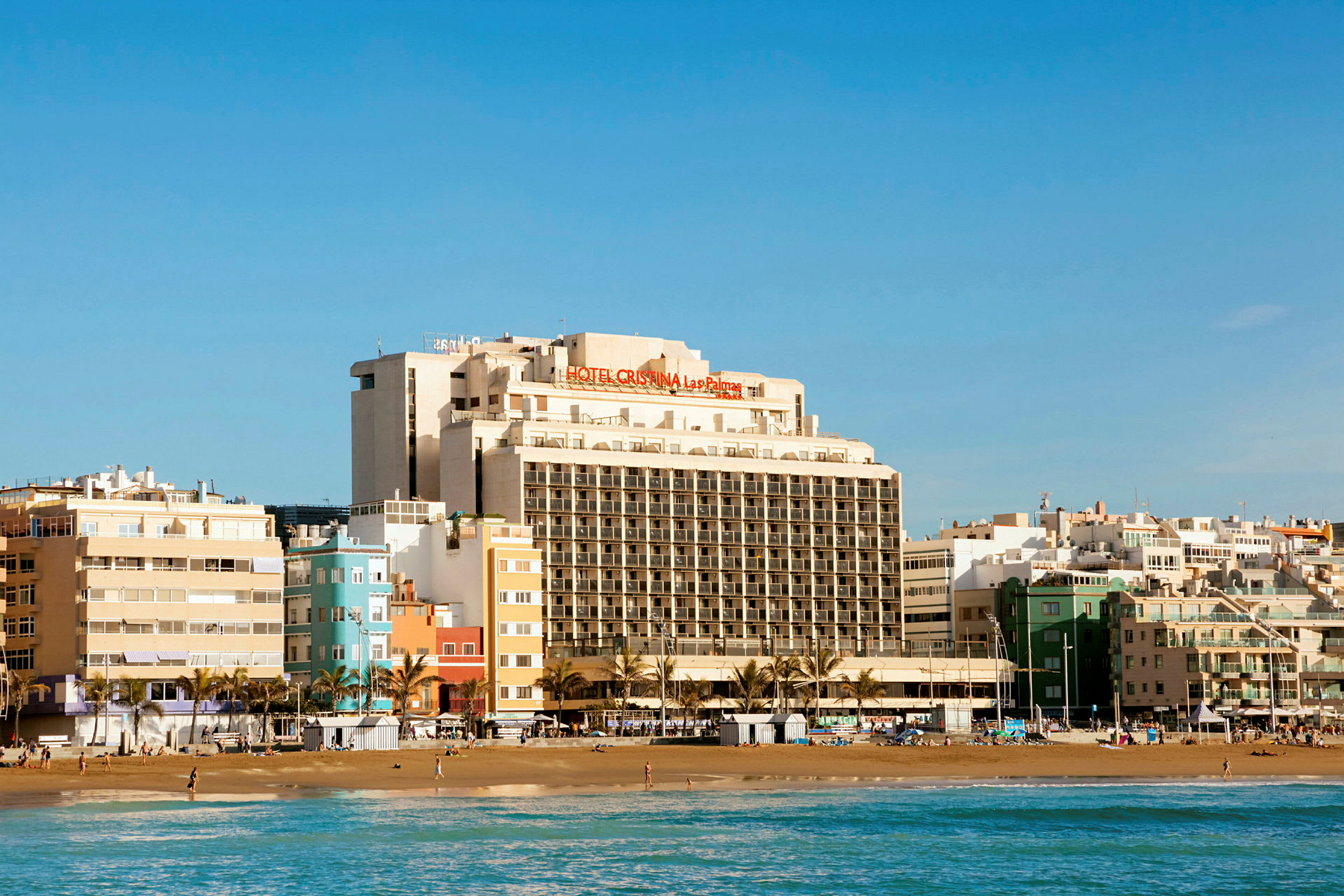 Utsikt over en strand med et stort hotellbygg i bakgrunnen. (AI-generert tekst)