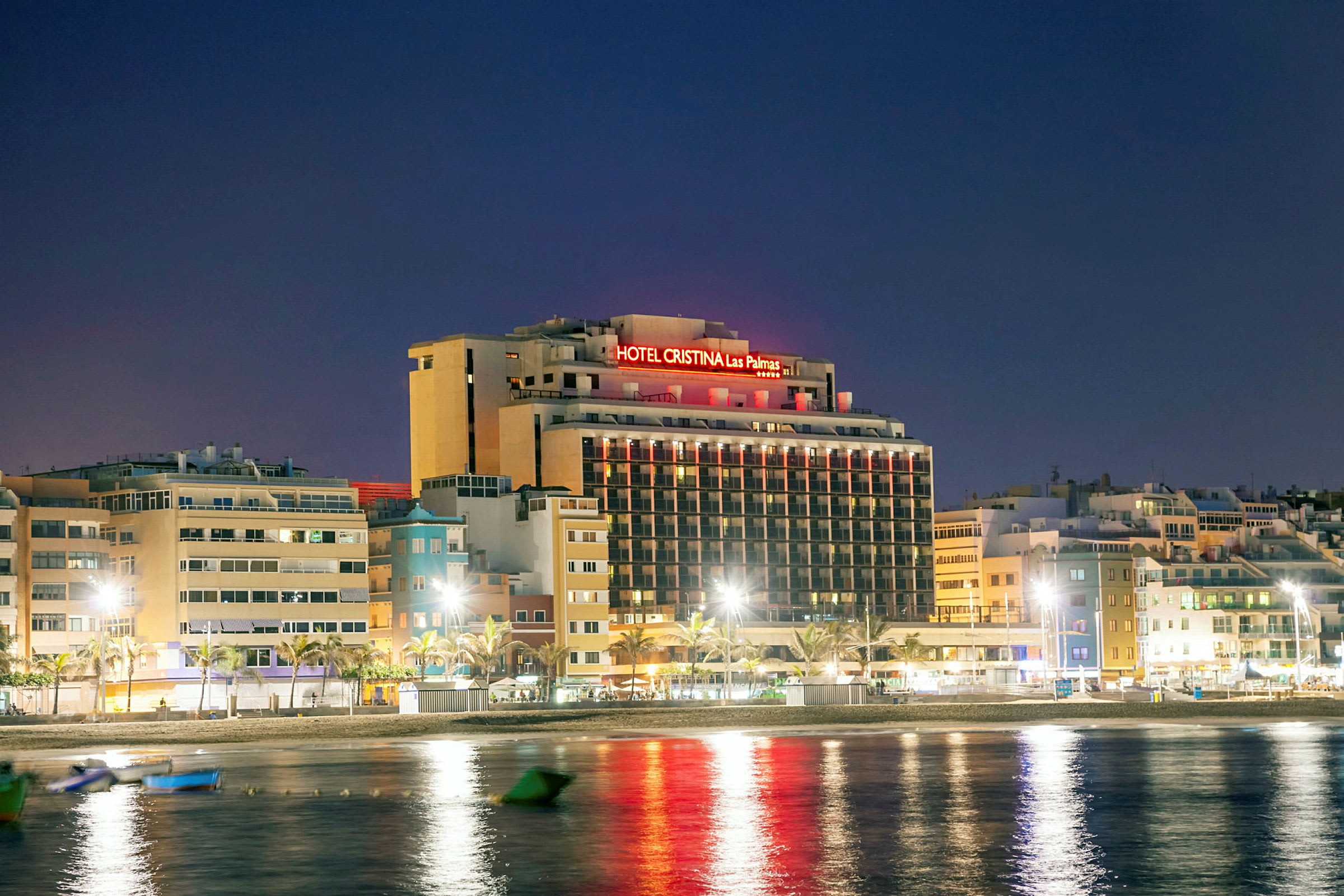 Bilde av hotellbygning med neonlys i nattmiljø, plassert nær vann. (AI-generert tekst)