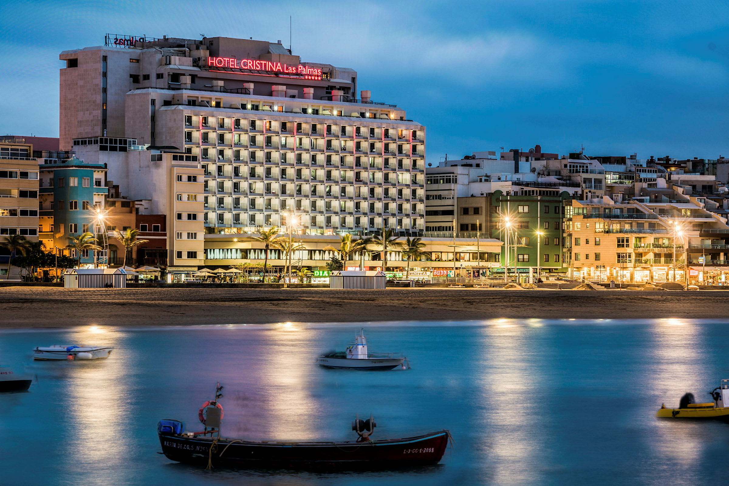 Hotellbygning nær strand, båter på vann i forgrunnen. (AI-generert tekst)