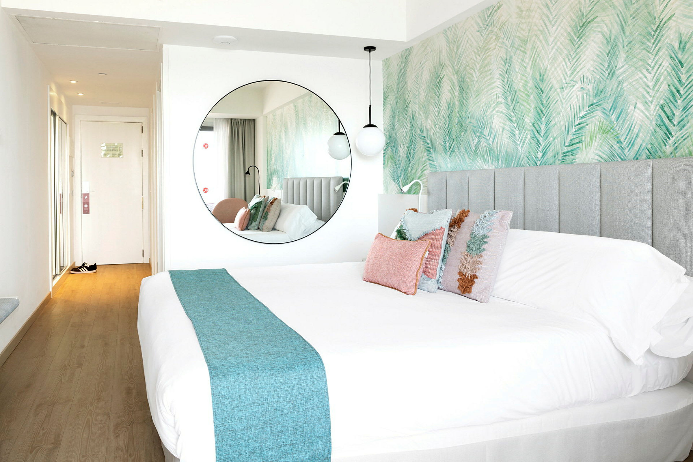 Et hotellrom med en stor seng og dekorative puter, samt et rundt speil på veggen. (AI-generert tekst)