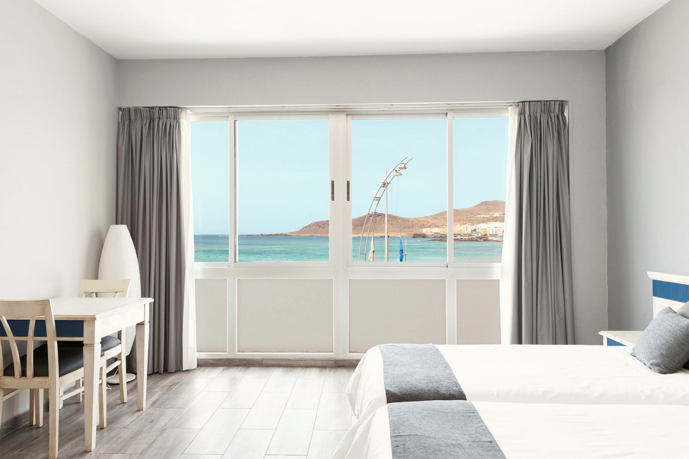 Lyst hotellrom med utsikt over havet gjennom en stor vindusfront. (AI-generert tekst)