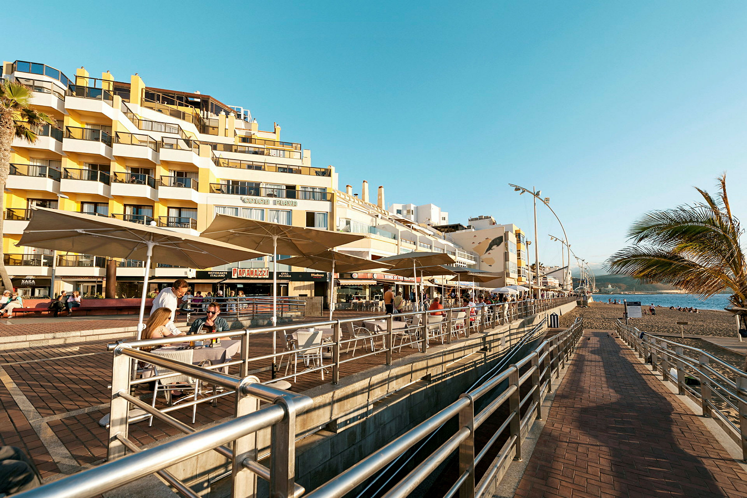 En strandpromenade med kafeer og et flerfamiliekompleks i bakgrunnen. (AI-generert tekst)