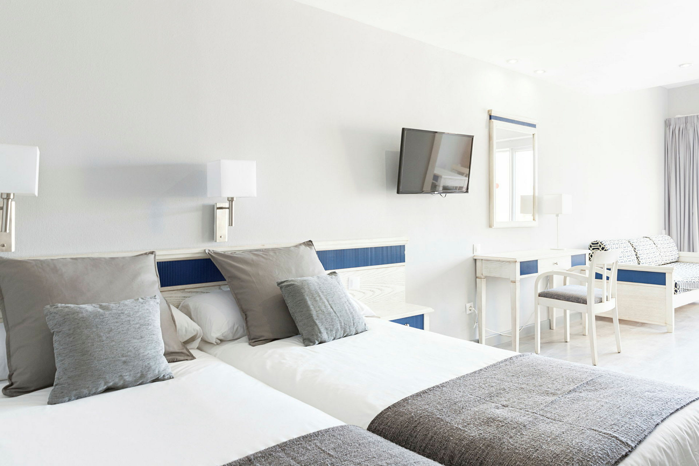 Hotellrom med to enkeltsenger, skrivebord, stol og veggmontert TV. (AI-generert tekst)