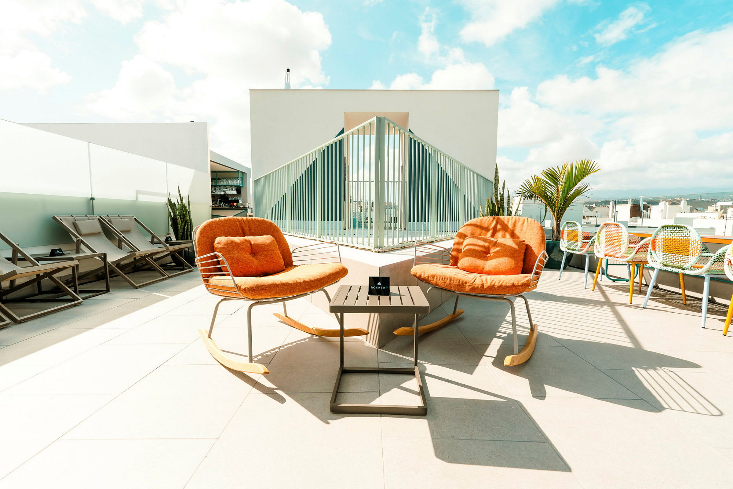 To orange gyngestoler med ryggstøtte står foran et bord på en takterrasse. (AI-generert tekst)