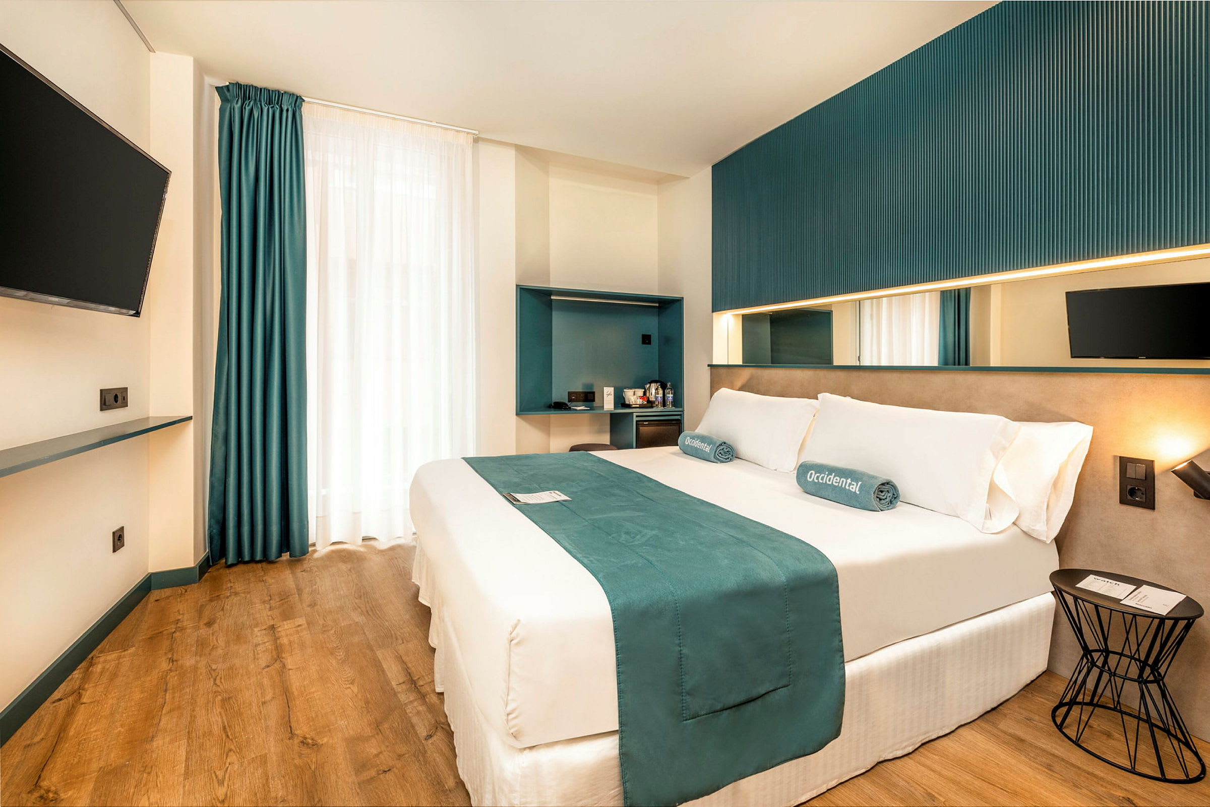 Et moderne hotellrom med en dobbeltseng, veggmontert TV og minimalistisk interiør. (AI-generert tekst)
