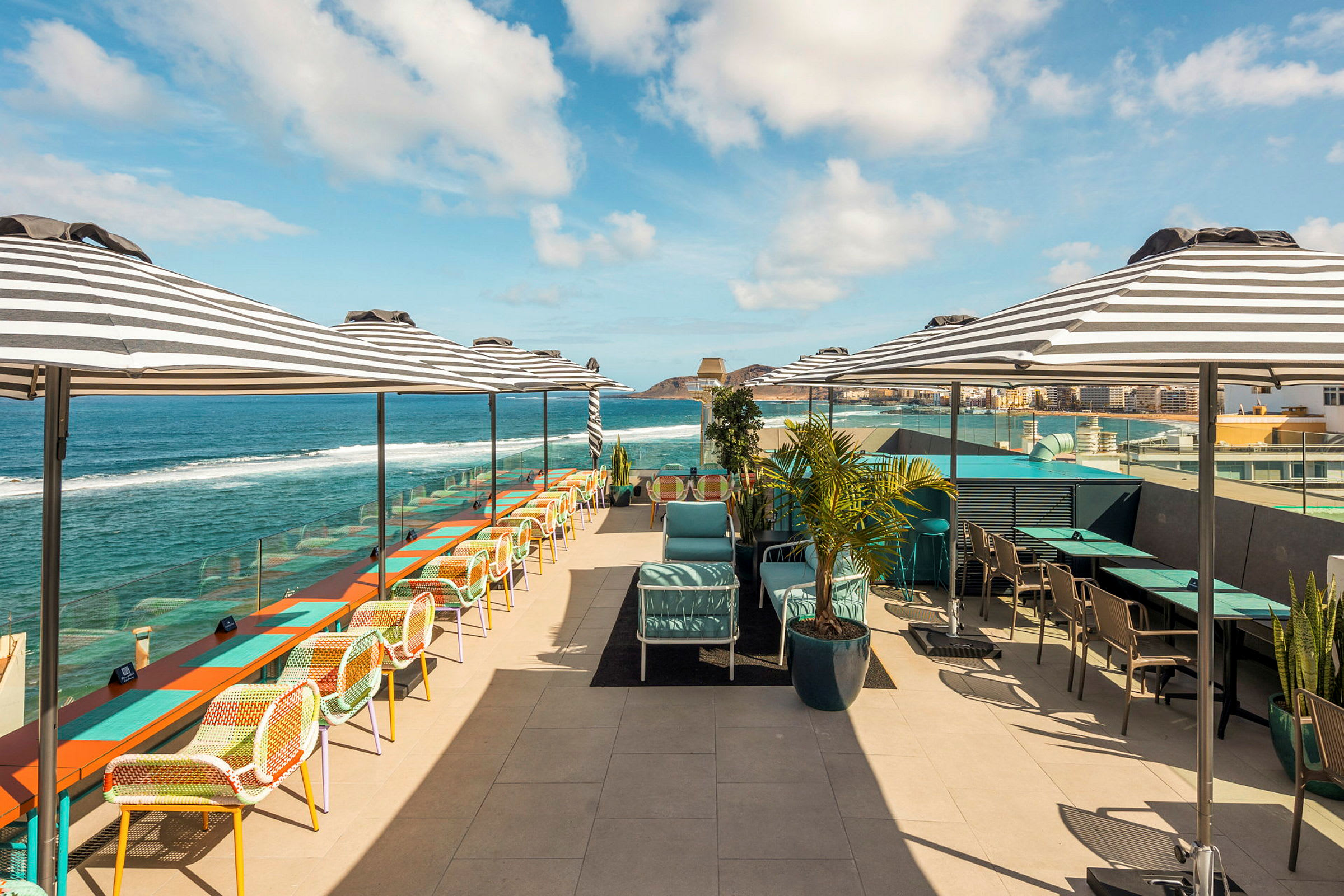 Takterrasse med sitteplasser, bord og parasoller, med utsikt over havet. (AI-generert tekst)