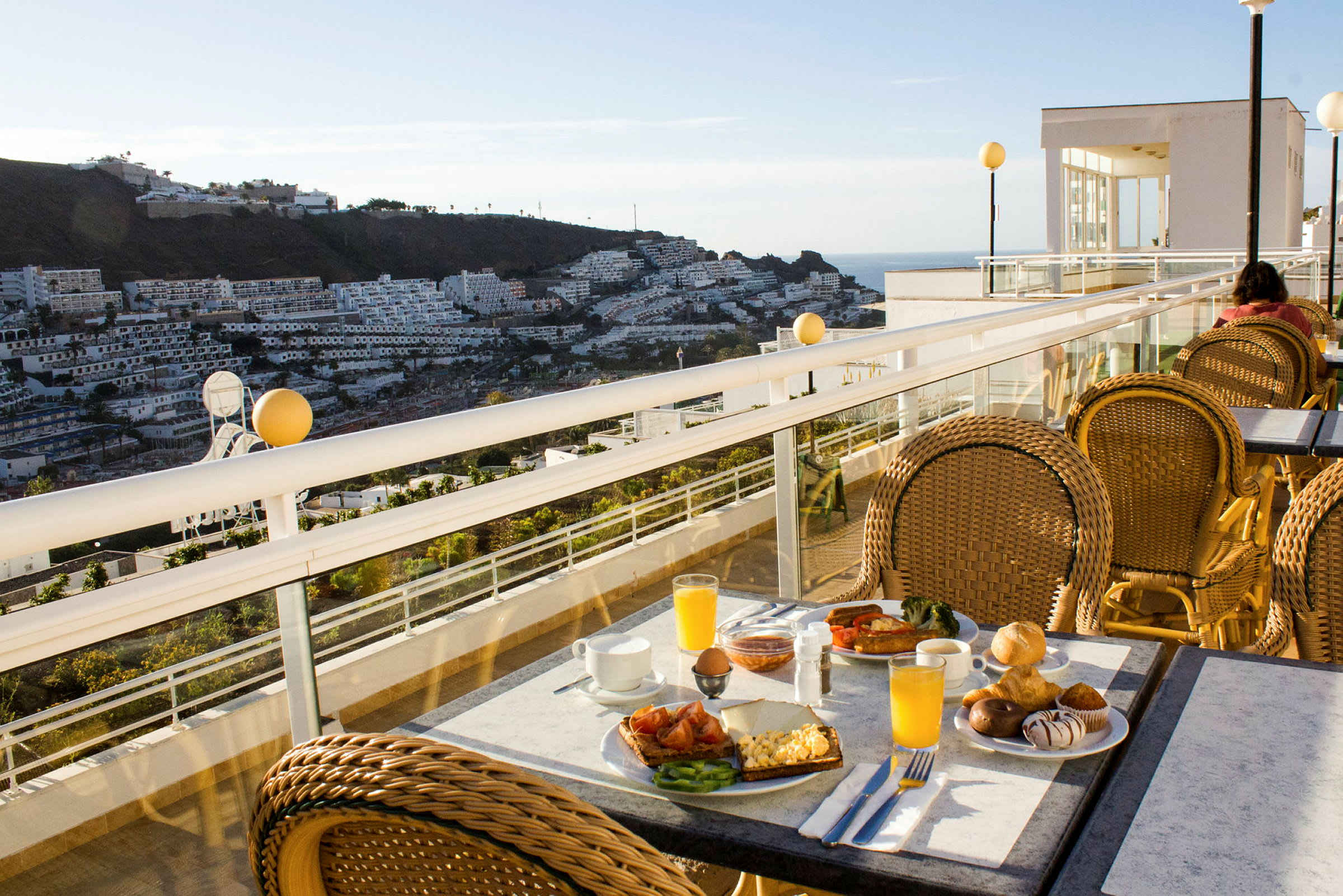 Utsikt fra en terrasse med frokostmåltid på et bord og boligbygninger i bakgrunnen. (AI-generert tekst)