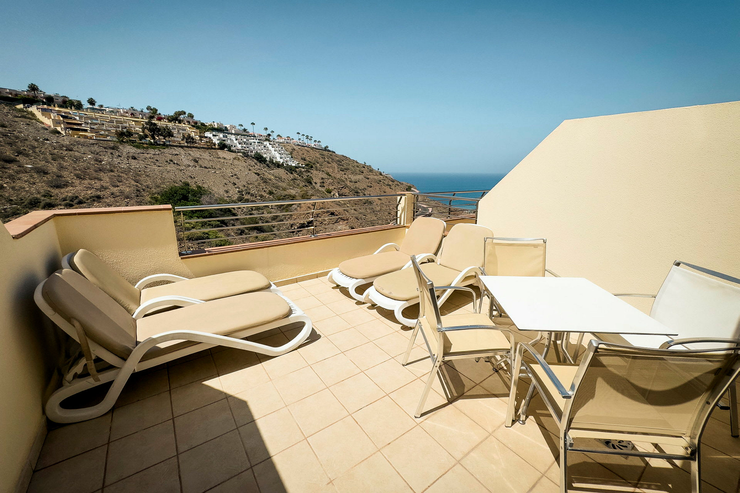 Terrasse med solsenger og bord med stoler, utsikt mot havet. (AI-generert tekst)