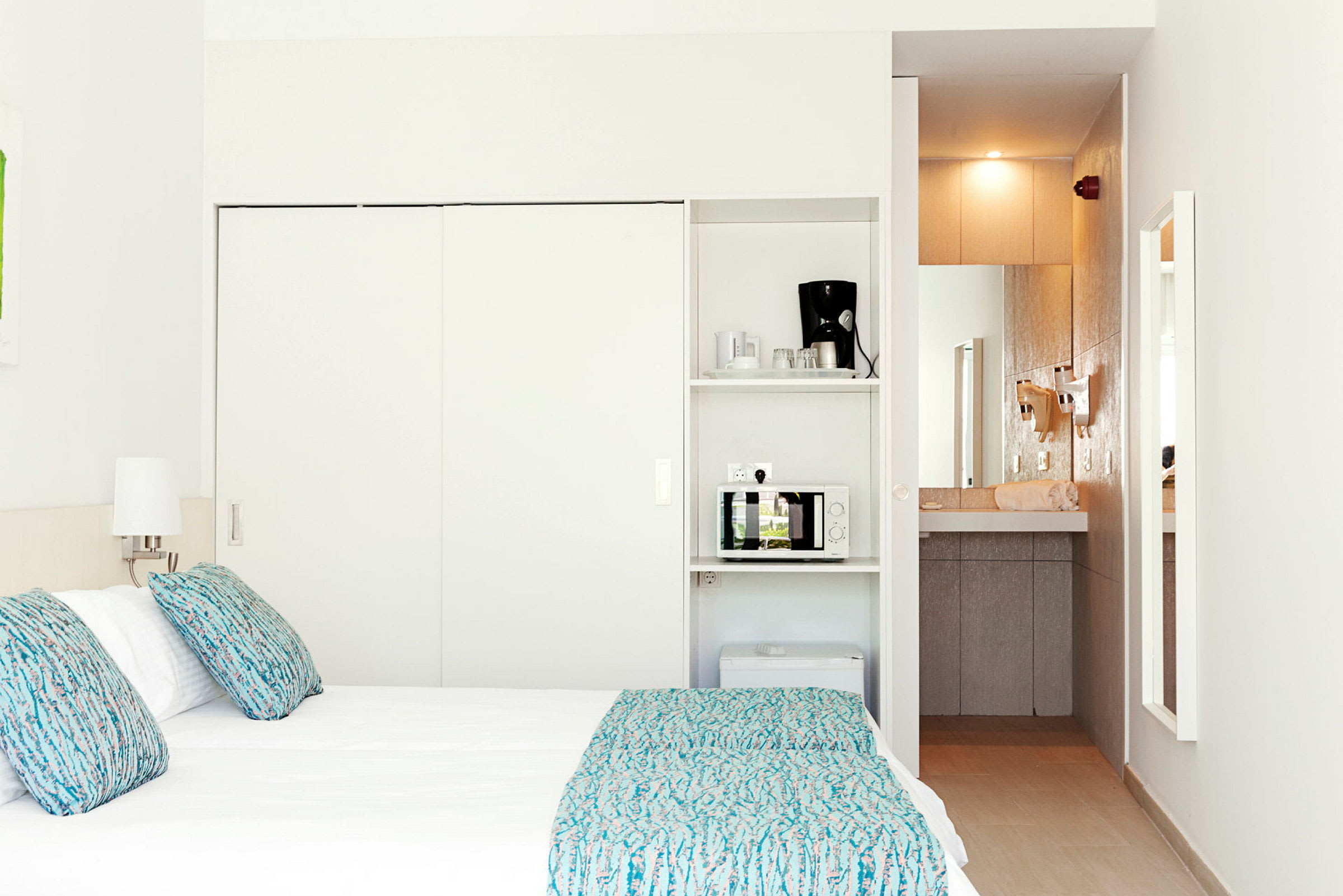 Et hotellrom med en seng, lamper og et minikjøkken som inkluderer en mikrobølgeovn og en kaffemaskin. (AI-generert tekst)