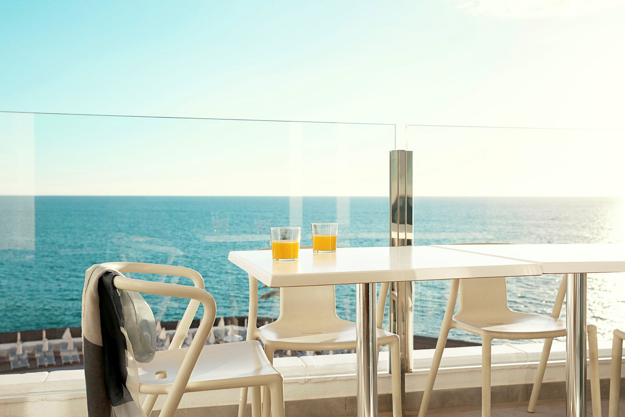 Bord med to glass appelsinjuice på en terrasse med utsikt over havet. (AI-generert tekst)