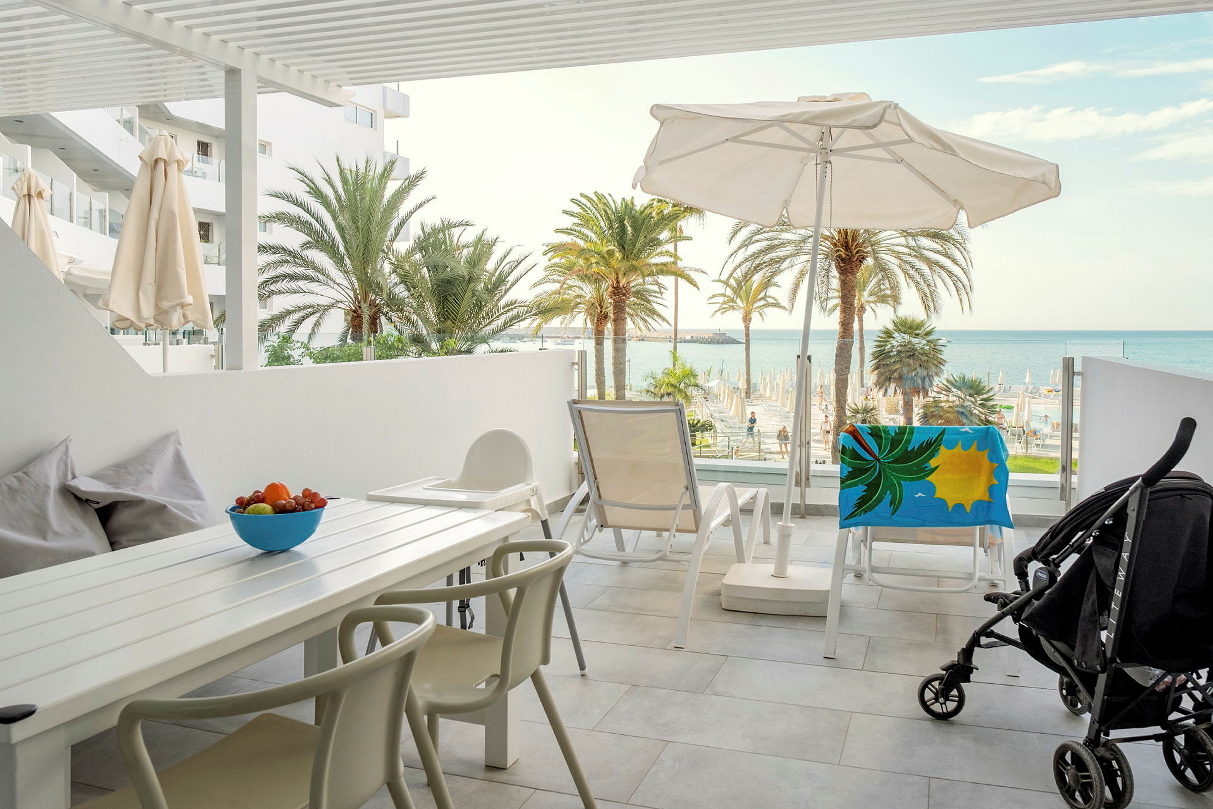 Utsikt fra en møblert terrasse mot havet og palmer. (AI-generert tekst)