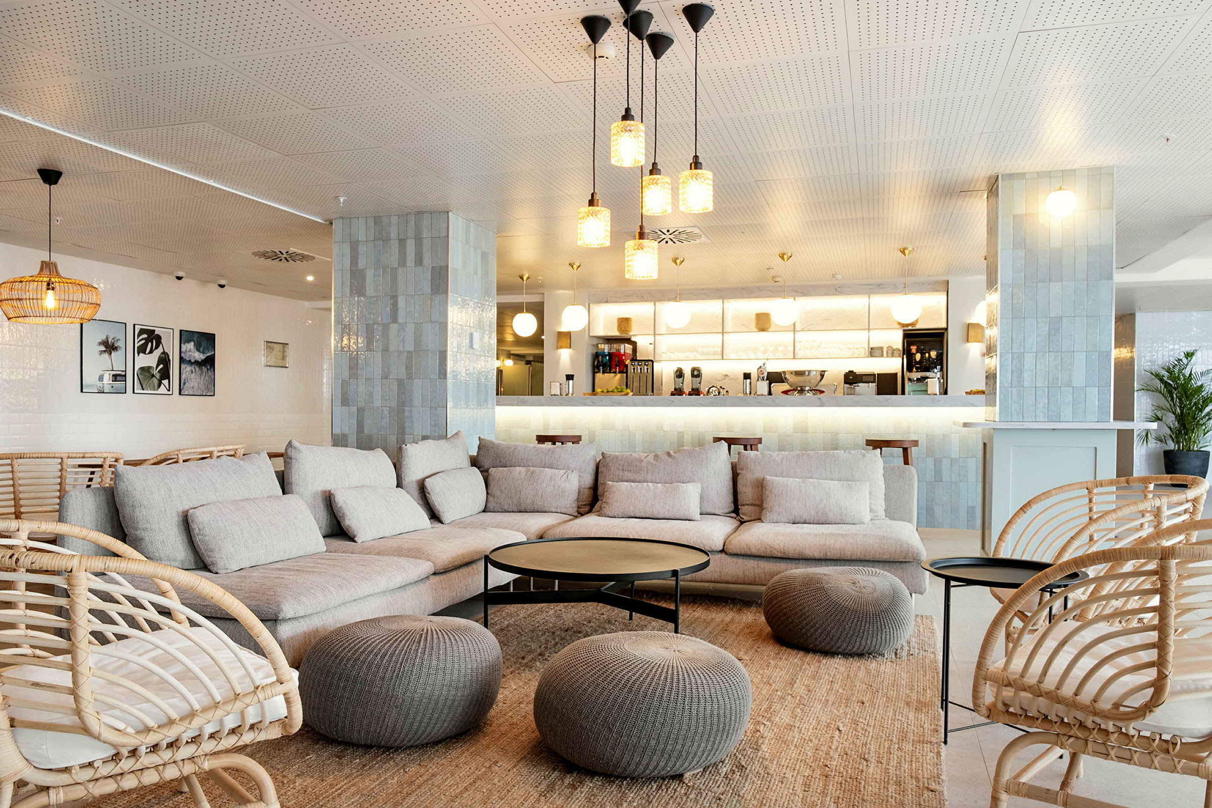En moderne lounge med beige sofaer og kurvstoler, innredet med bord og dekorasjoner samt en kaffebar i bakgrunnen. (AI-generert tekst)