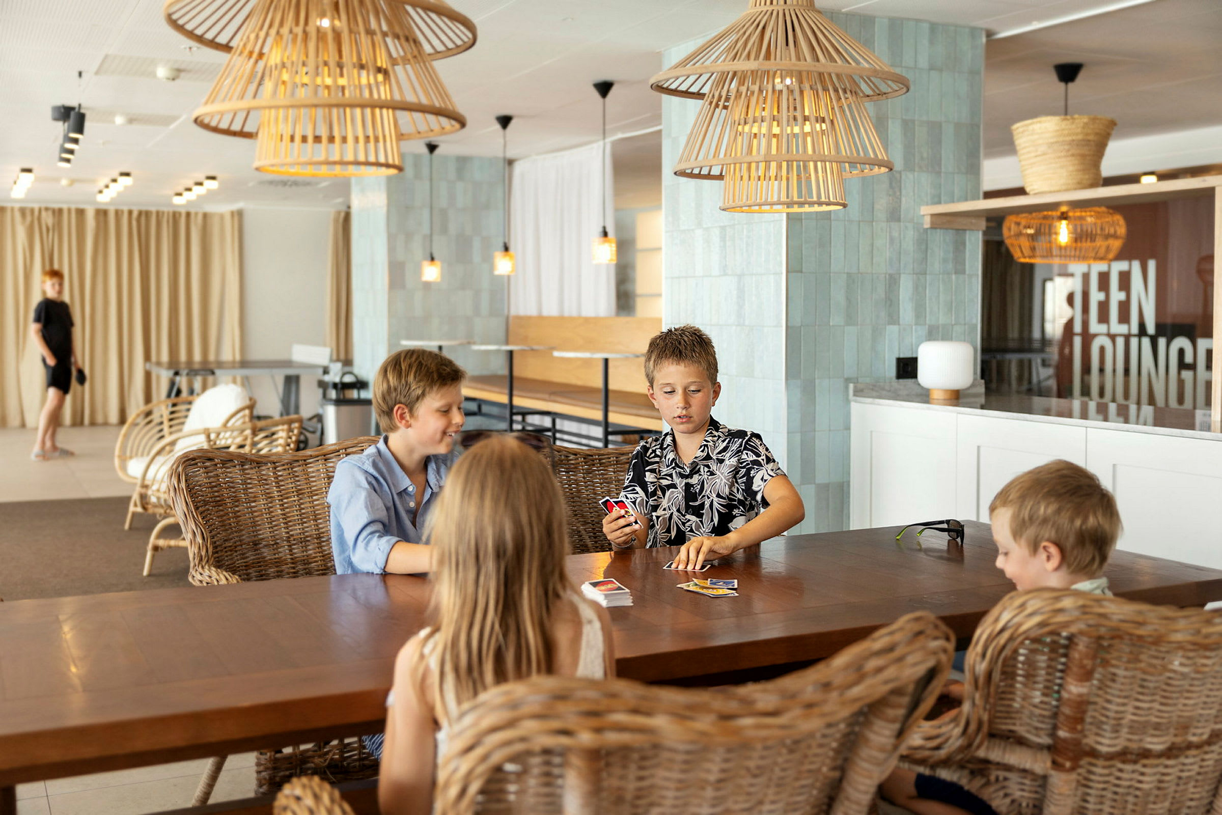 Fire personer sitter ved et bord og spiller kort i en moderne lounge. (AI-generert tekst)