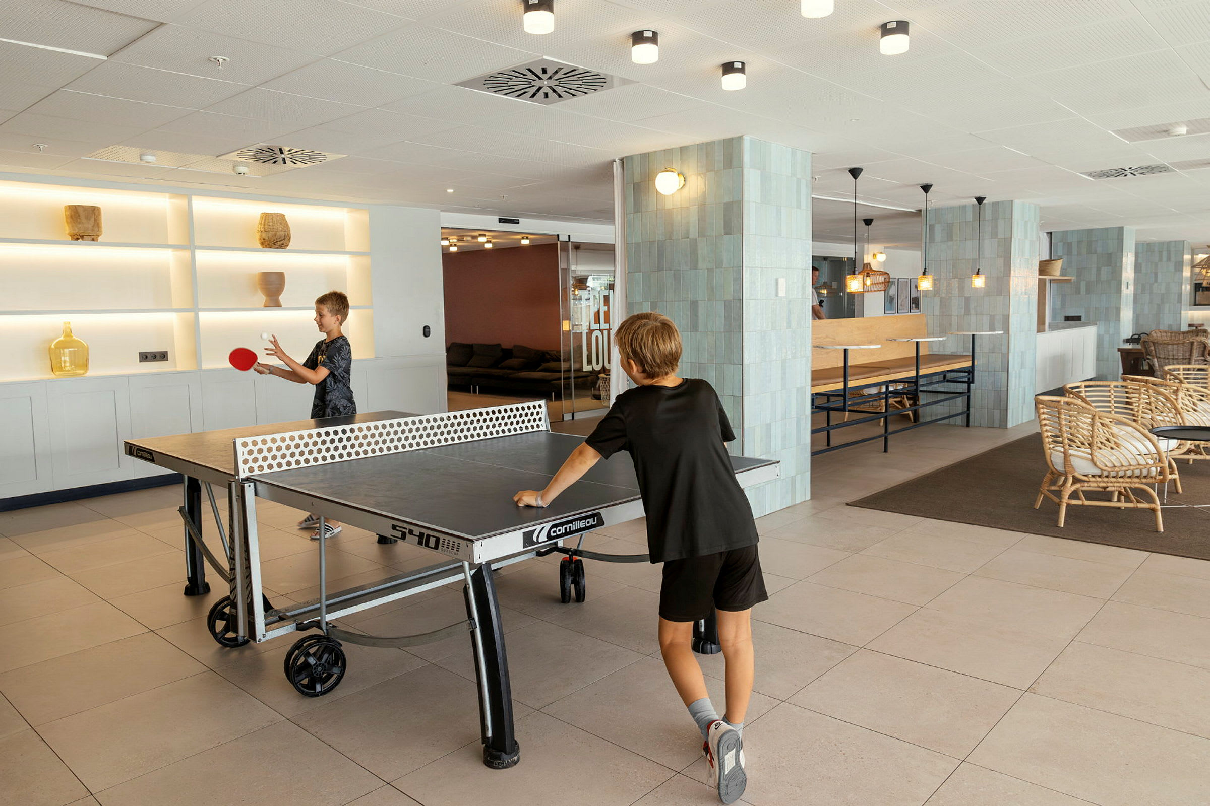To personer spiller bordtennis i et lyst innredet fellesområde. (AI-generert tekst)