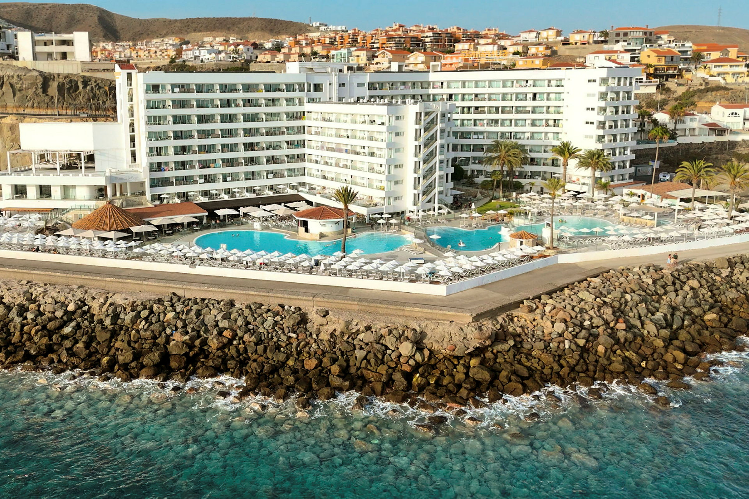 Hotell ved kysten med flere bassenger og solsenger. (AI-generert tekst)