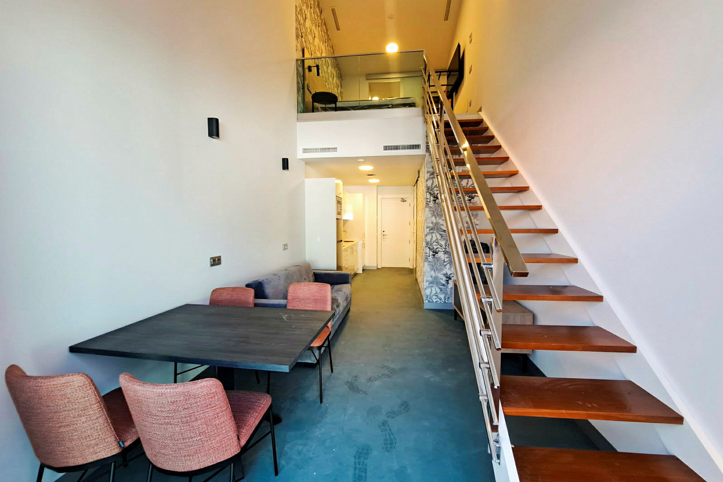 Bilde av et moderne loft med en trapp, et spisebord og stoler, samt en liten kjøkkenkrok og sofa. (AI-generert tekst)