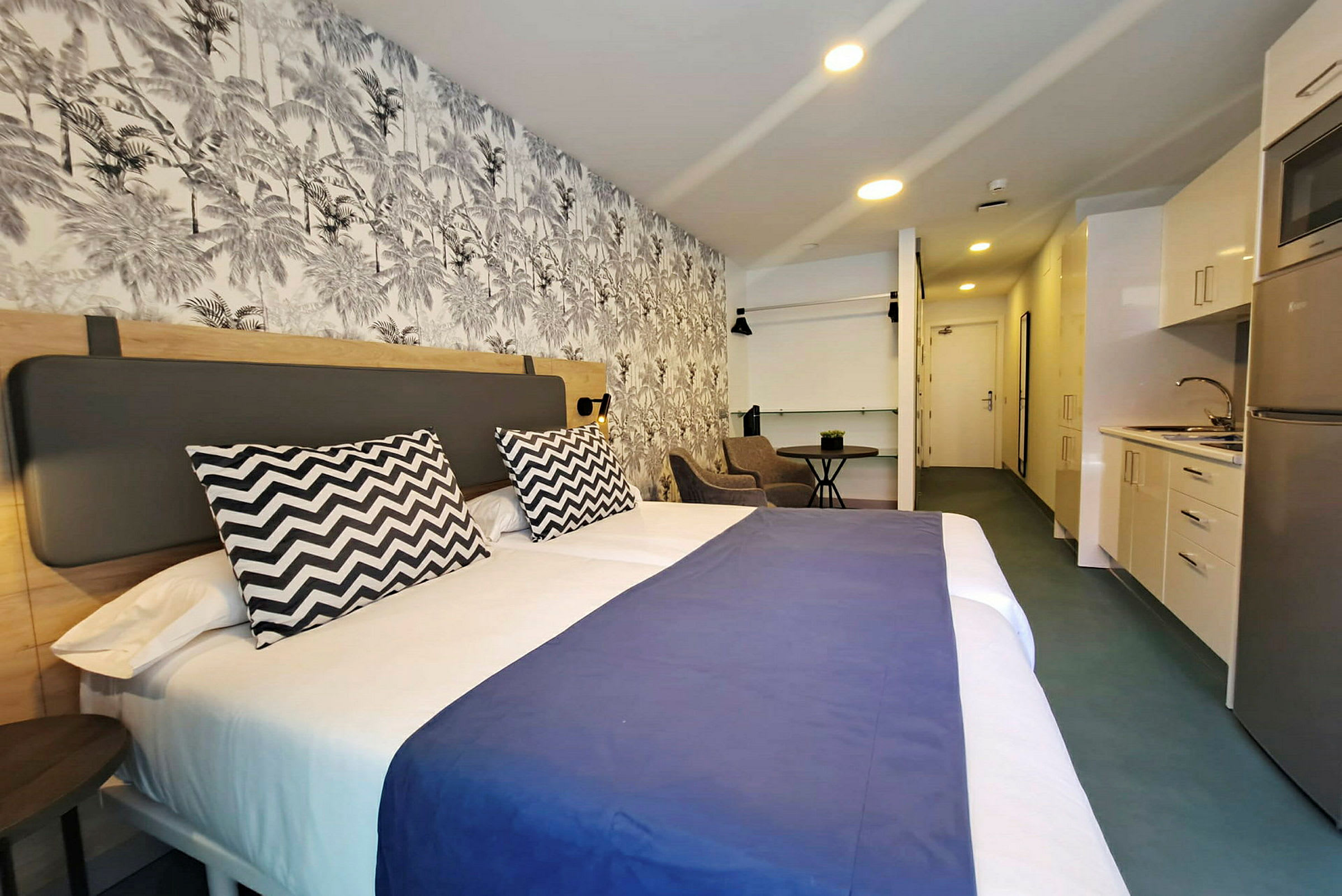 Hotellrom med en stor seng, dekorativ vegg og et lite kjøkken. (AI-generert tekst)